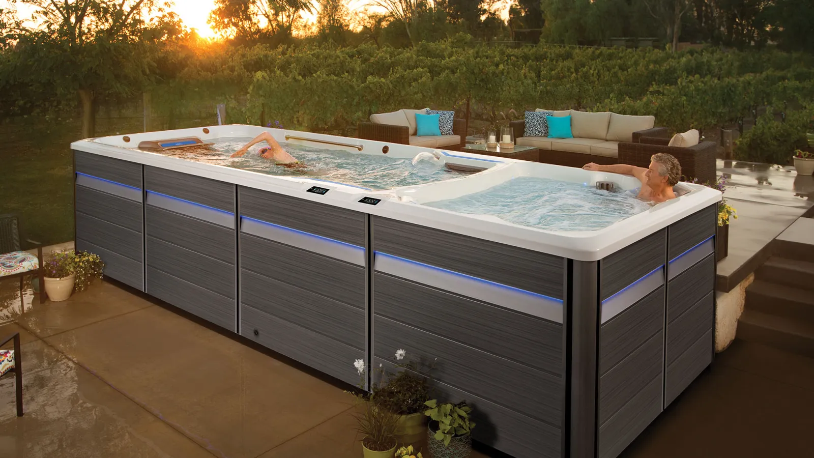 Modern outdoor swim spa with two people enjoying exercise and relaxation at sunset in backyard patio.