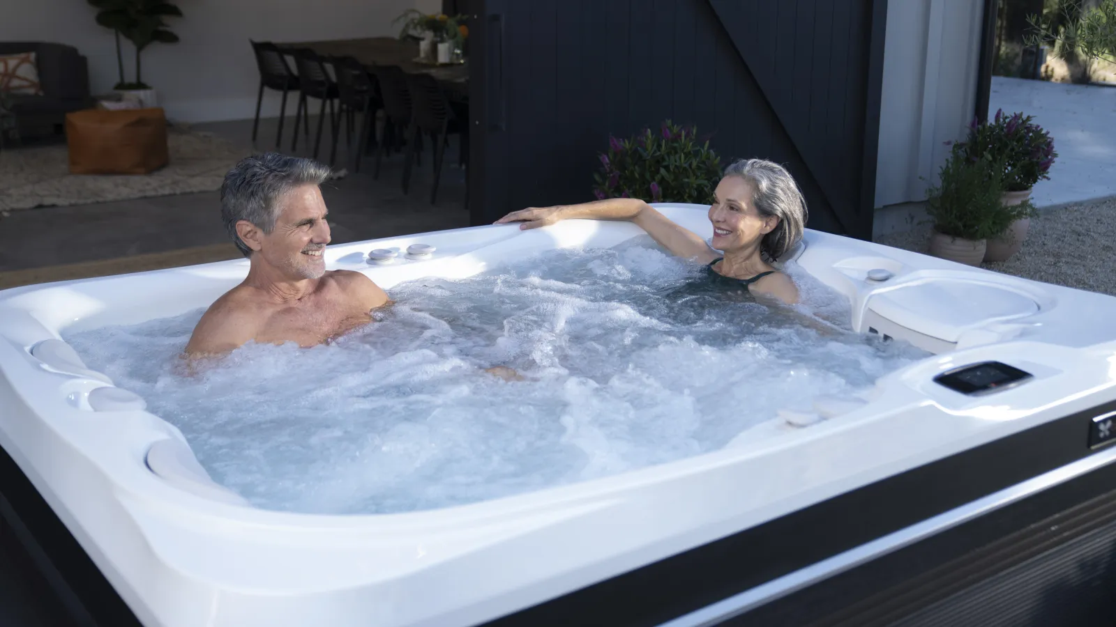 Mature couple relaxing and smiling in a bubbling outdoor hot tub on a sunny day.