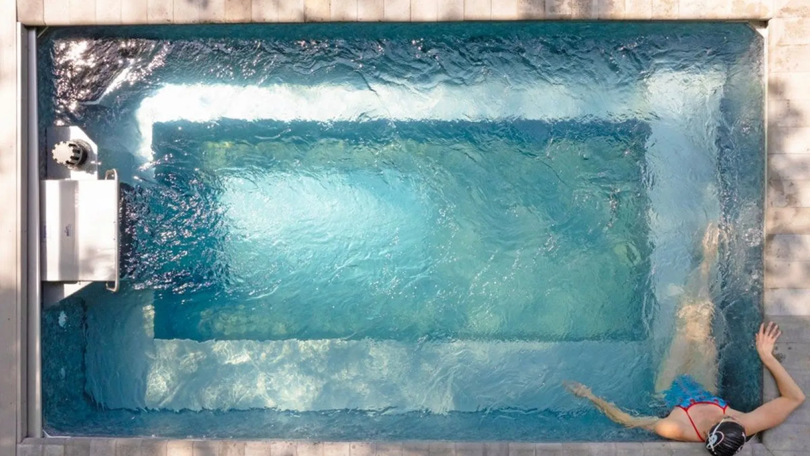 Top view of a person swimming in a small rectangular pool with clear blue water and tiled edges.