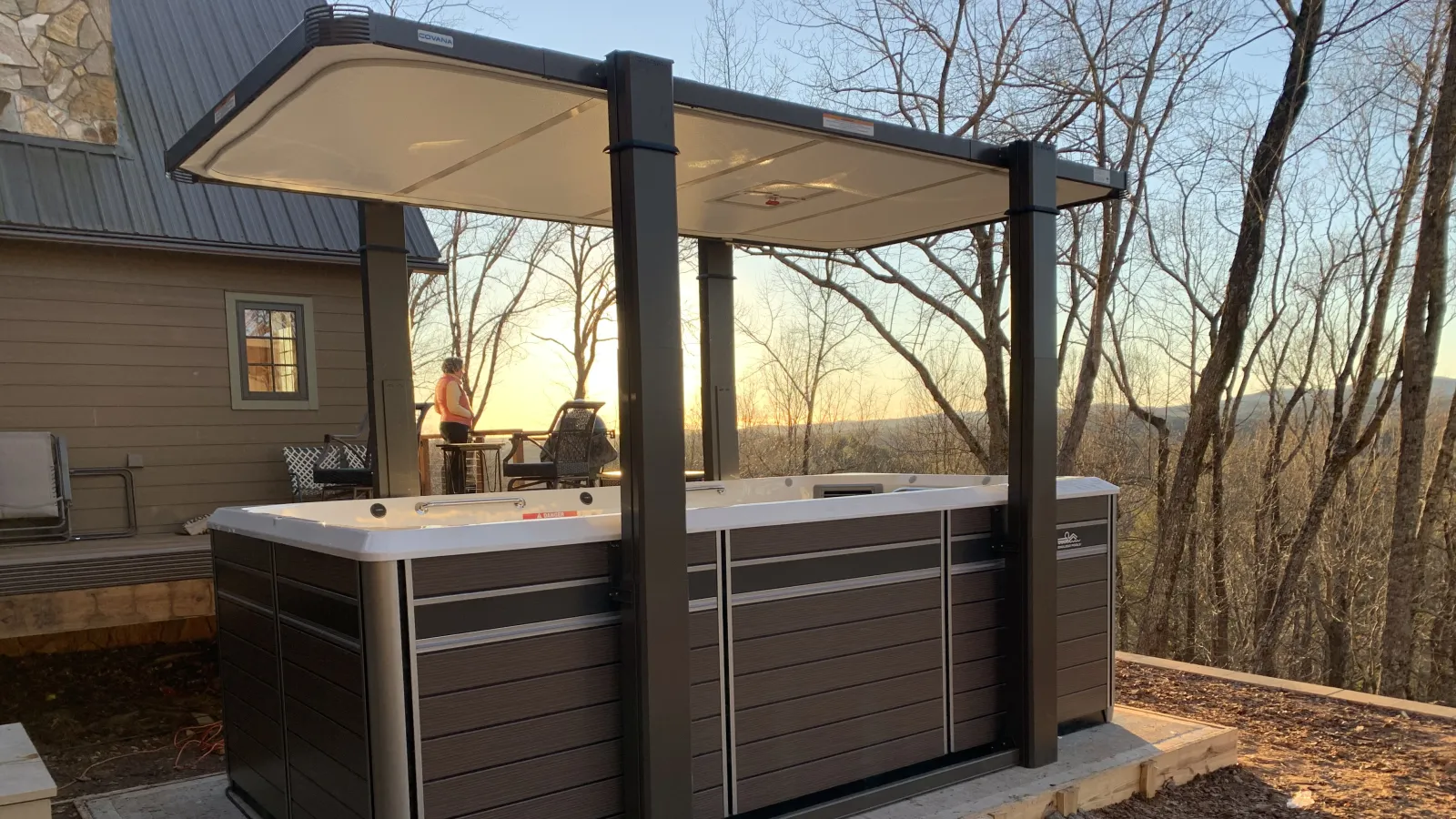 Modern outdoor hot tub with canopy on concrete pad during sunset in wooded backyard
