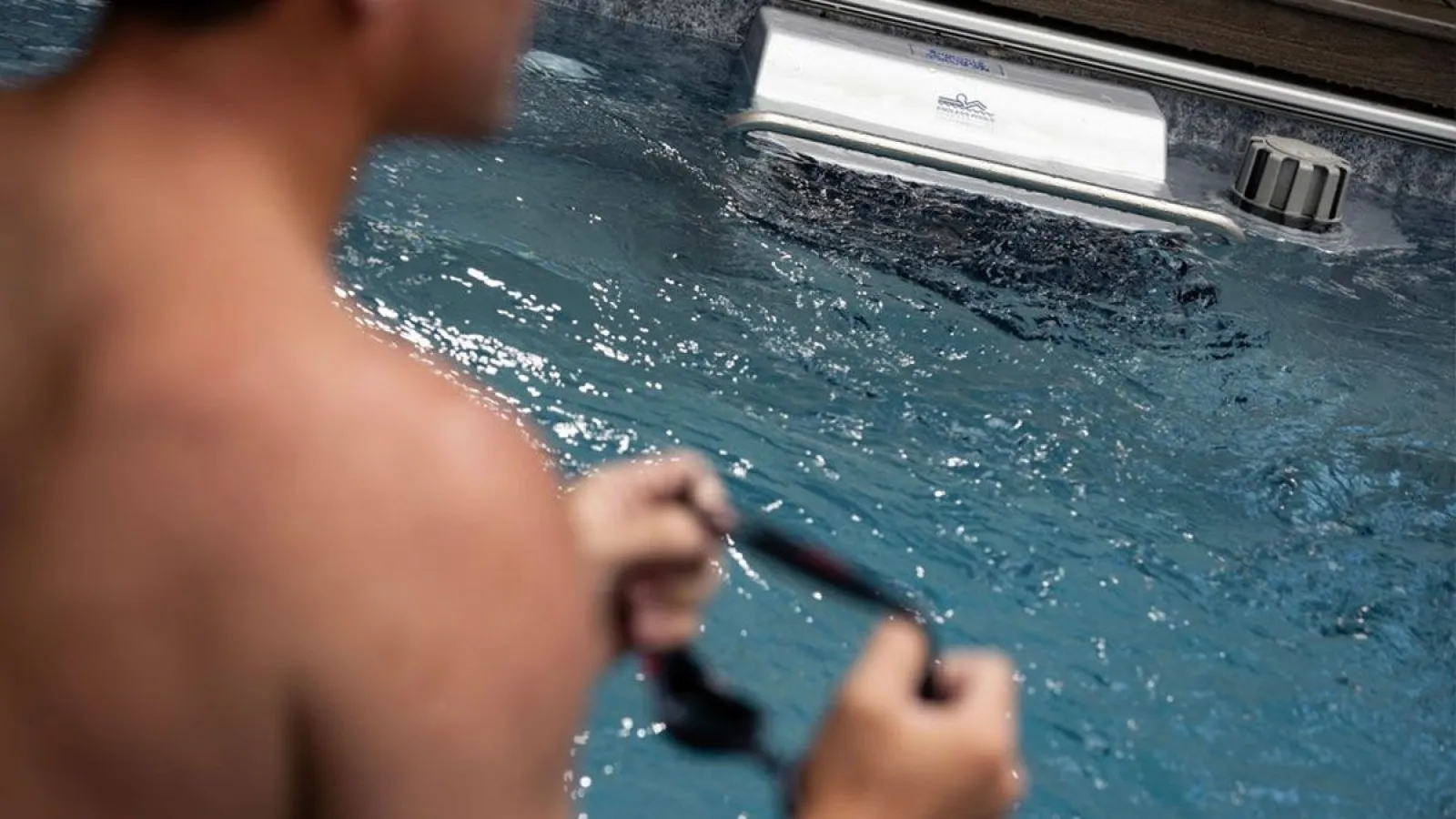Man holding sunglasses near the edge of a blue hot tub with bubbling water and wooden surroundings.