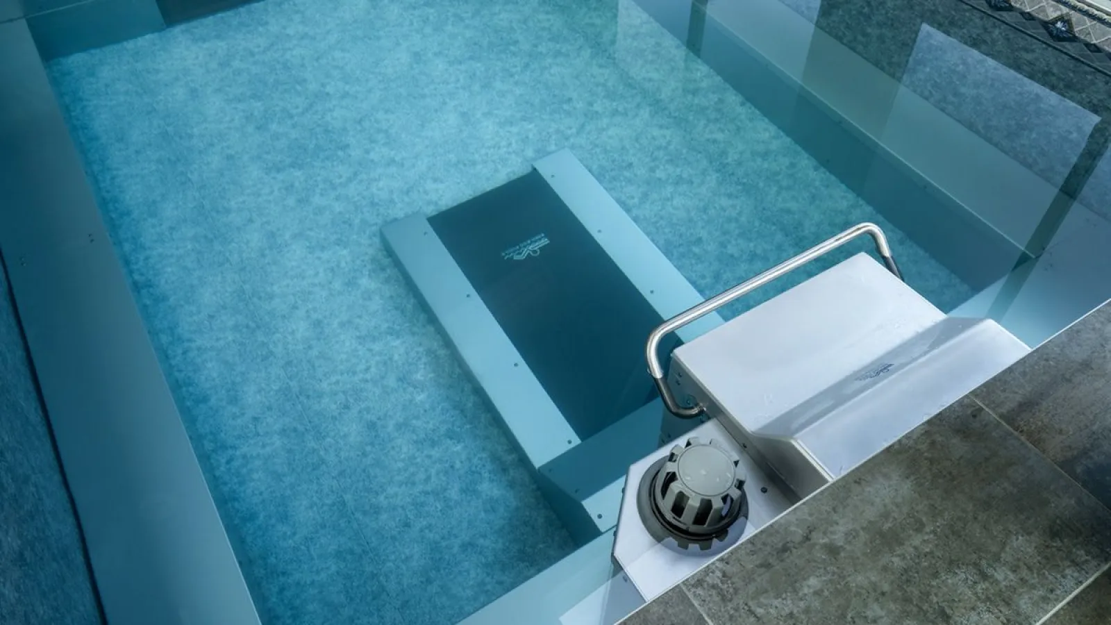 Modern robotic pool cleaner submerged in a clear swimming pool near the steps on a sunny day