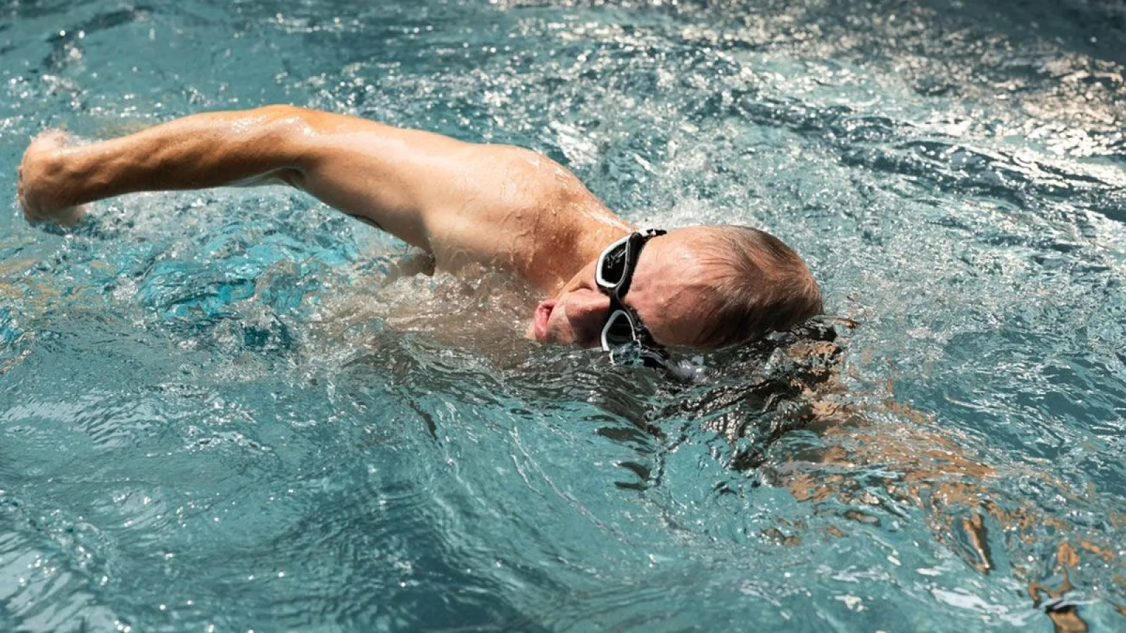 Man swimming freestyle stroke wearing goggles in clear blue water in a pool