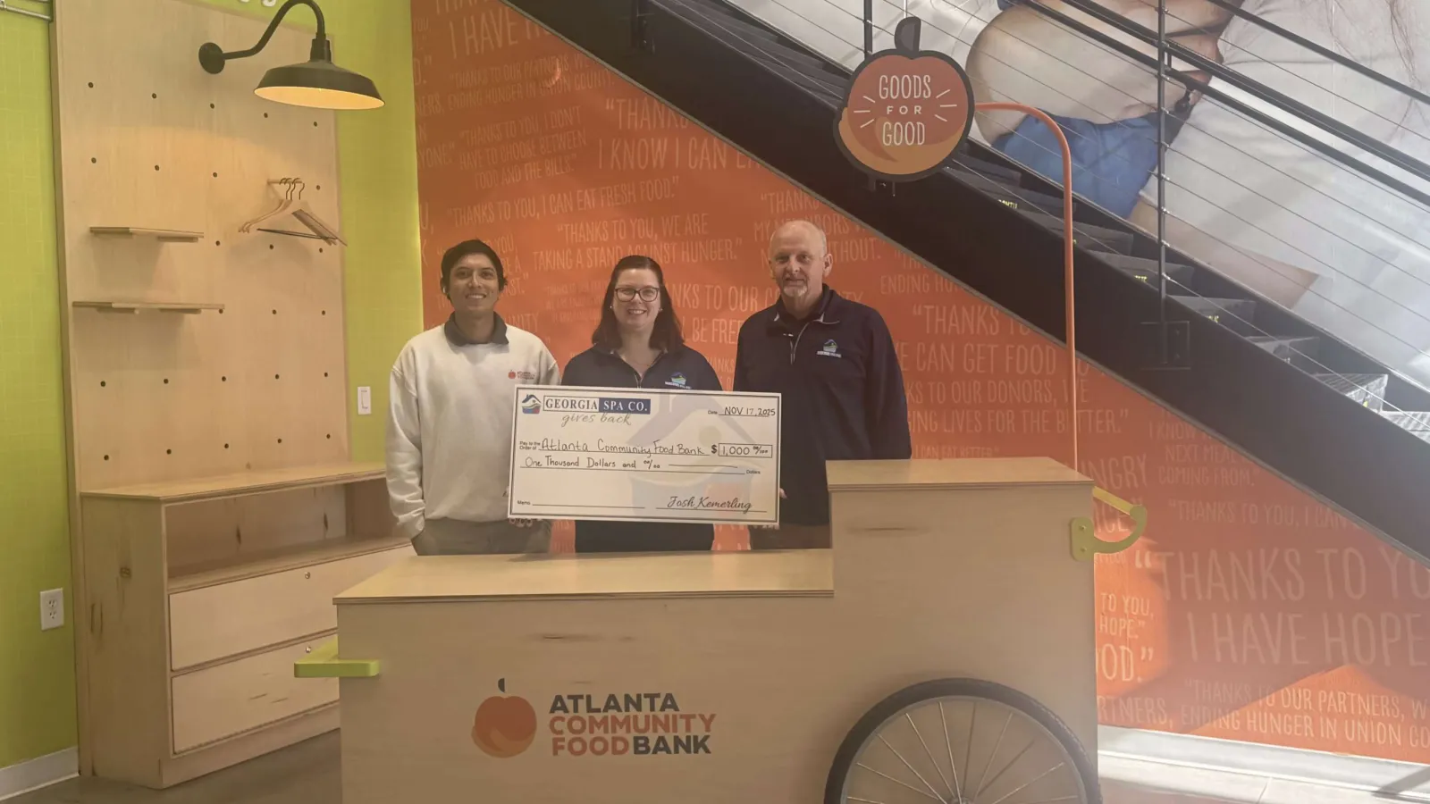 Three people holding a large donation check at Atlanta Community Food Bank with goods for good signage