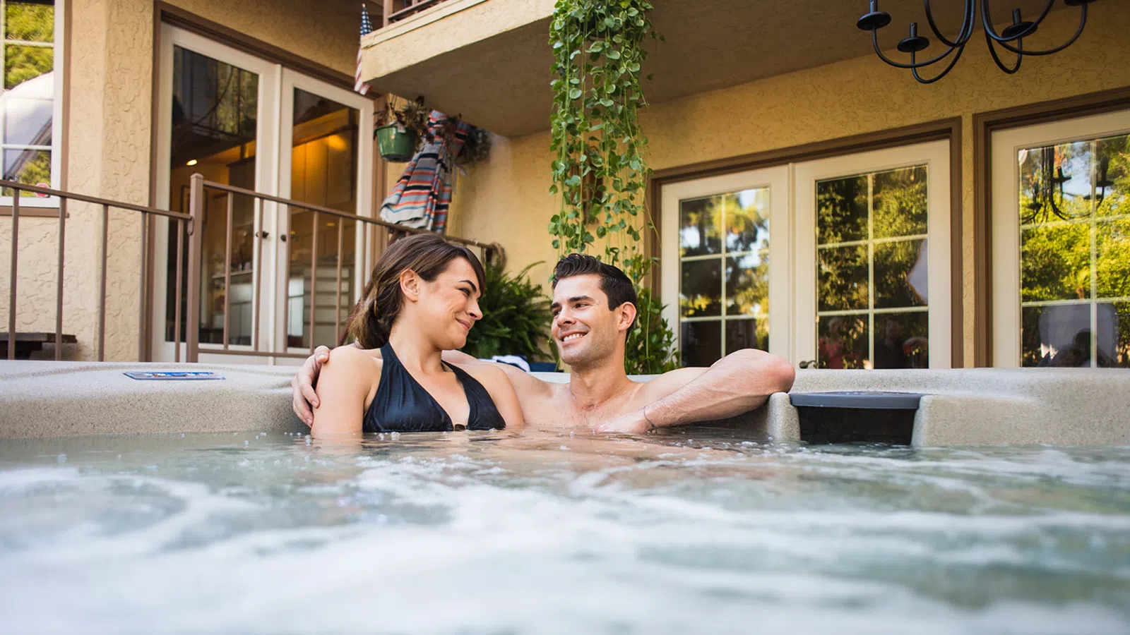 Couple enjoying a relaxing moment in a hot tub surrounded by lush greenery and sunlight.