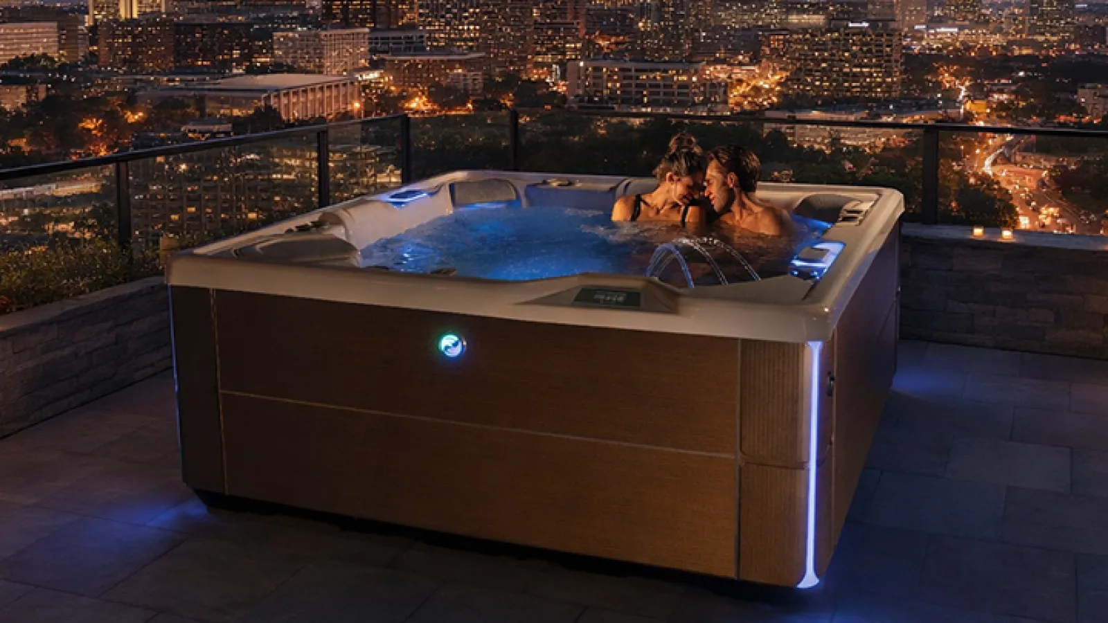 Couple relaxing in rooftop hot tub with city skyline and evening lights in the background