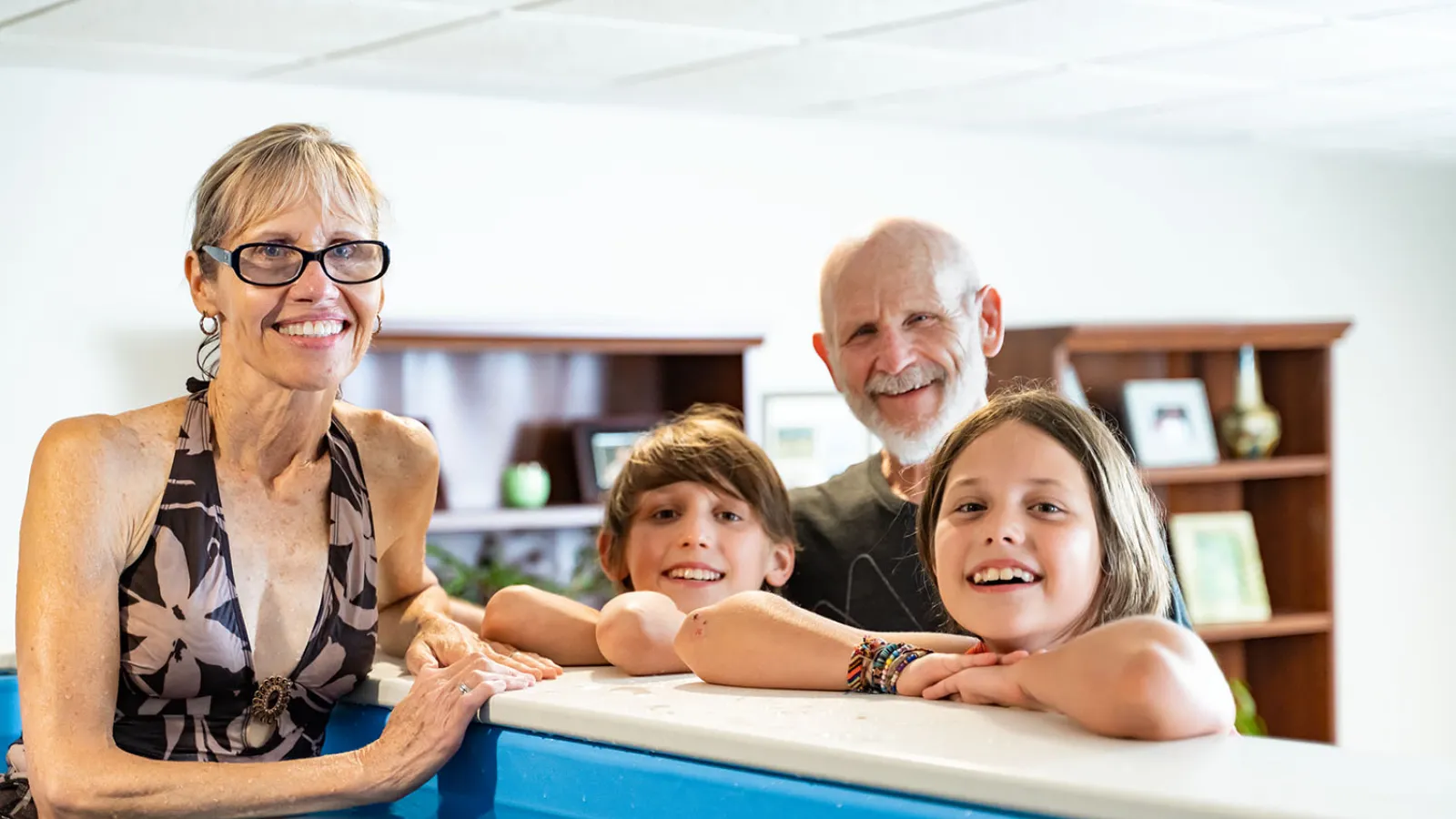 Smiling grandparents with grandchildren leaning on edge of indoor swimming pool in bright room