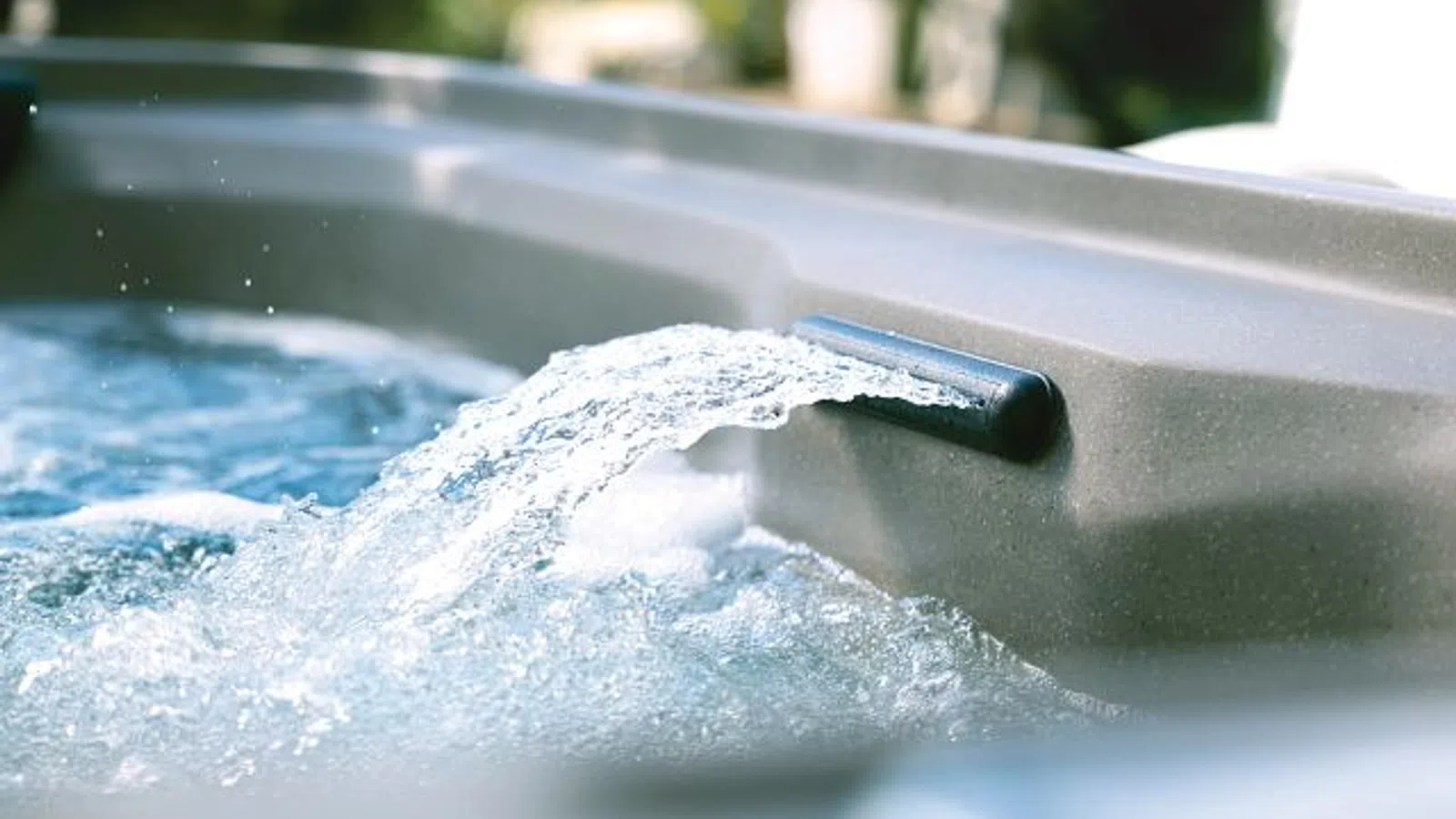 Water flowing from a spout into a bubbling hot tub with a blurred outdoor background