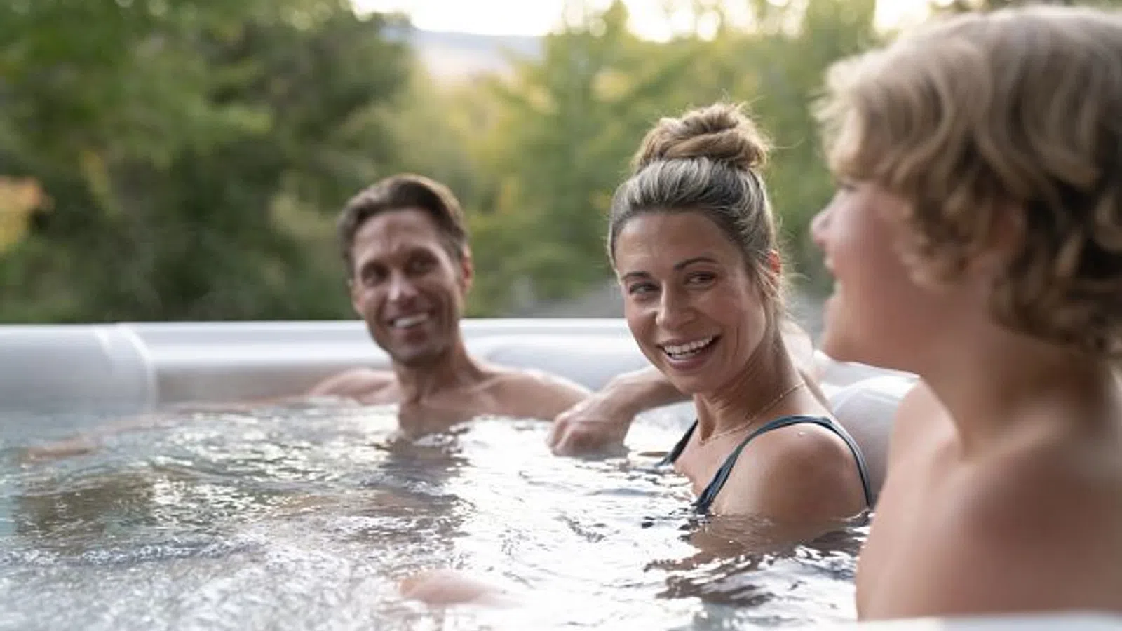 Three people enjoying a relaxing moment together in an outdoor hot tub surrounded by greenery.