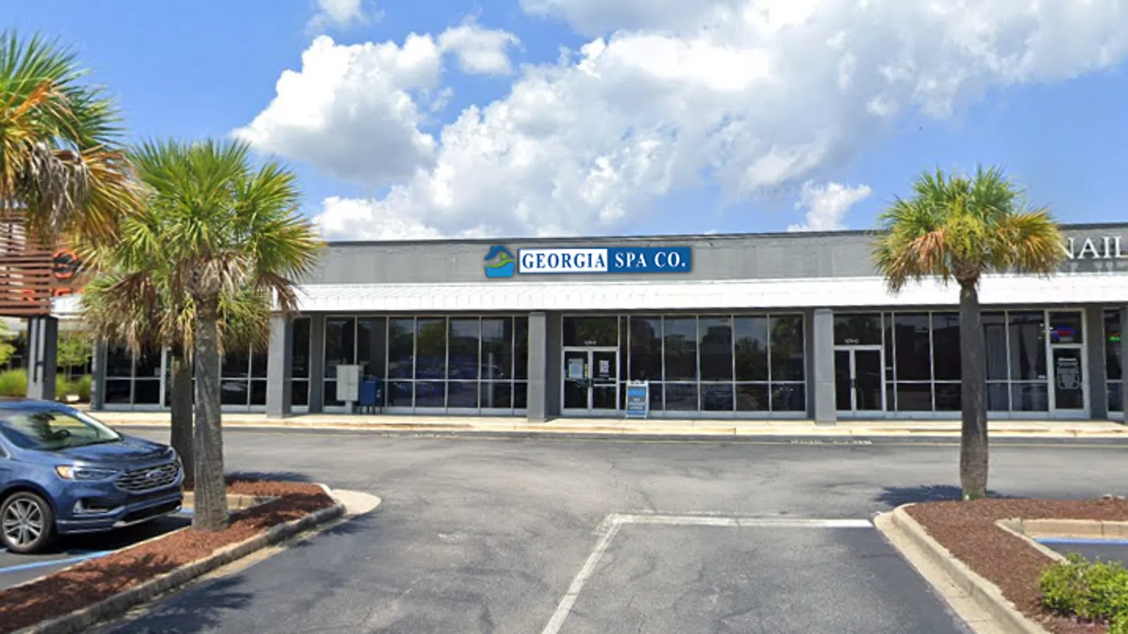 Exterior view of Georgia Spa Co. storefront with palm trees and parked cars under a blue sky.