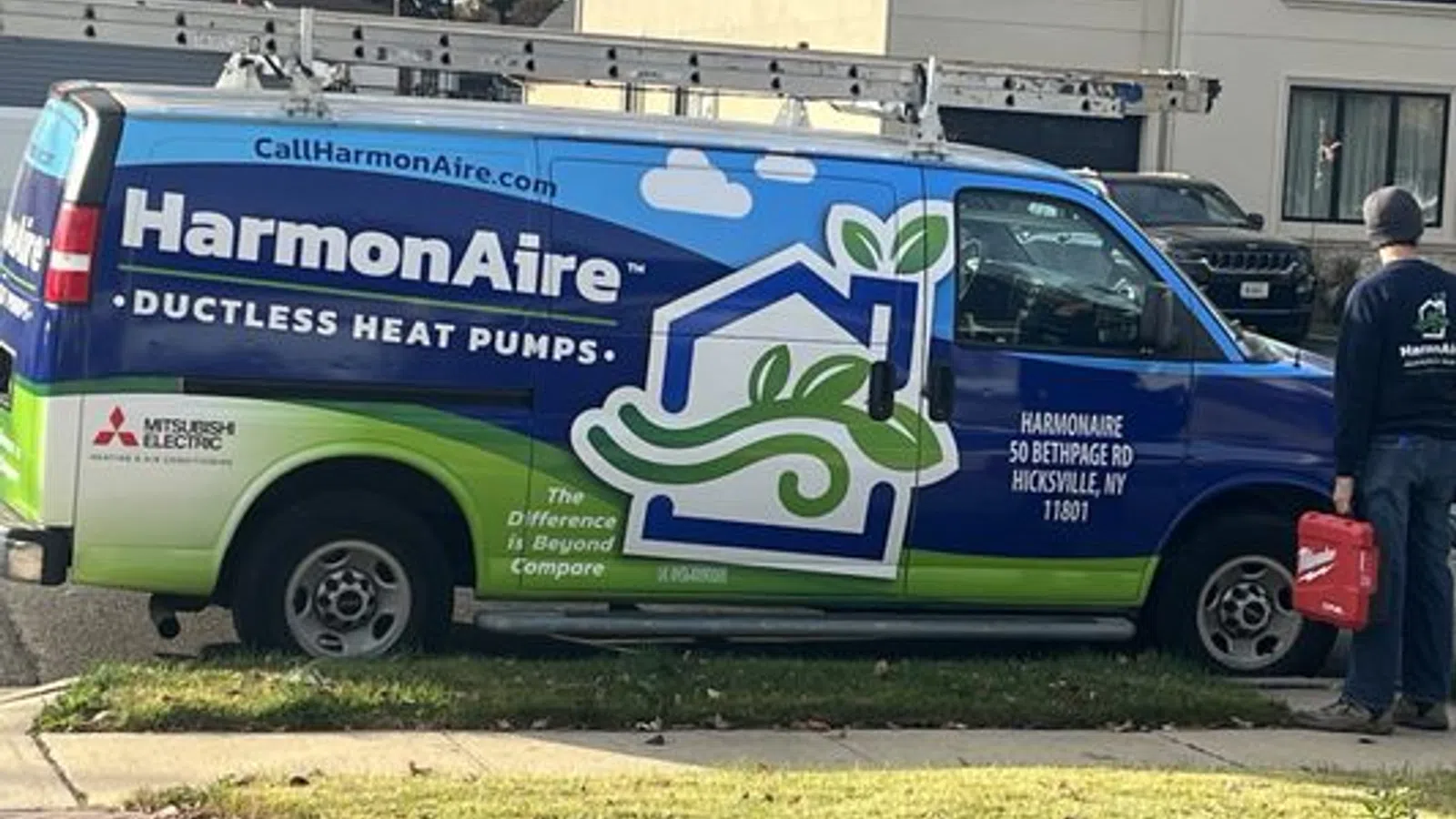 HarmonAire ductless heat pumps service van parked on street with technician holding red toolbox.