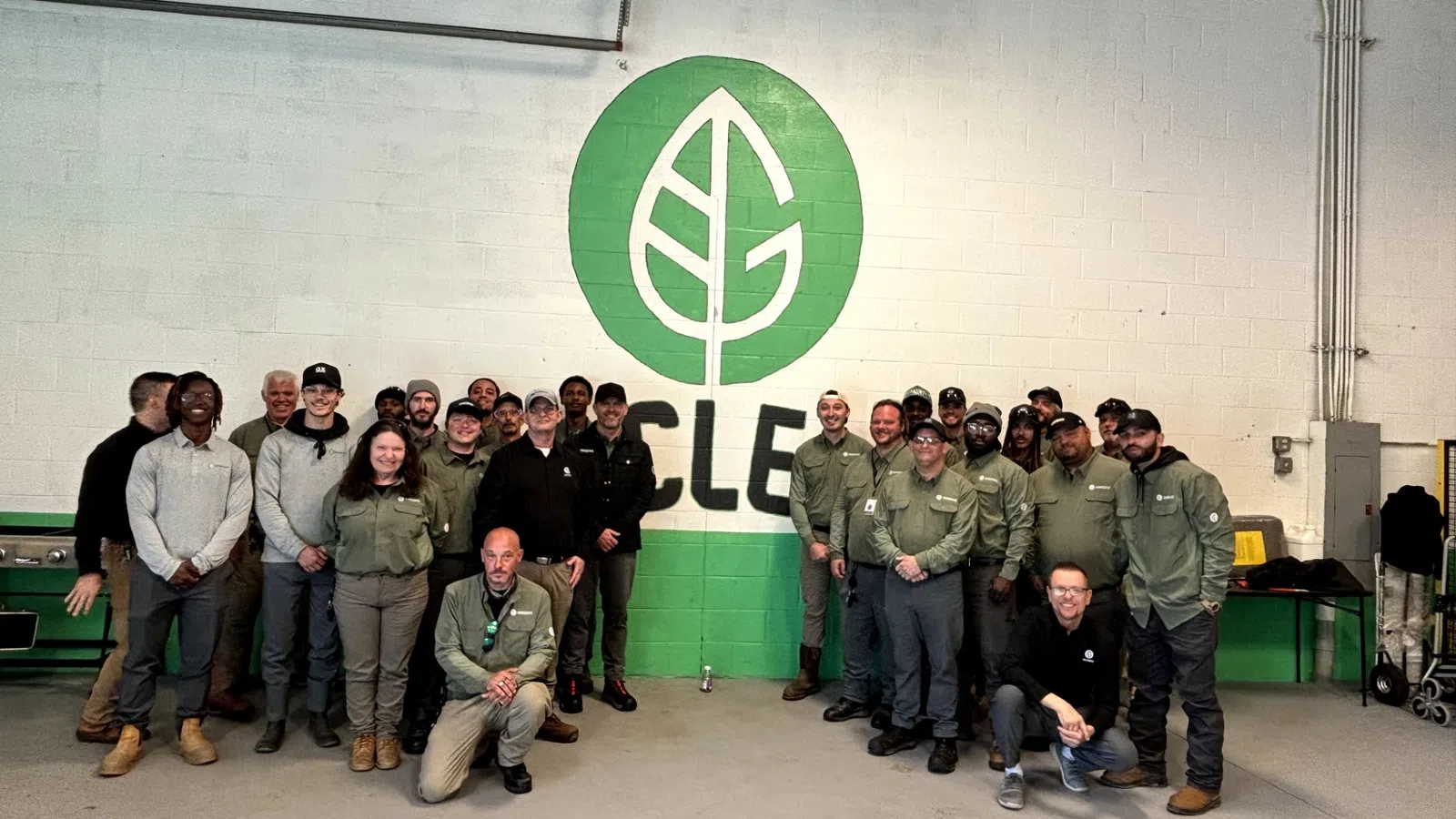 Group of employees posing in front of a green and white wall mural with a leaf logo and the word CYCLE
