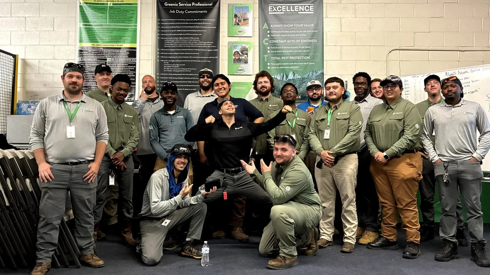 Group photo of Greenix pest control team in uniform inside office with company posters and logo on wall.
