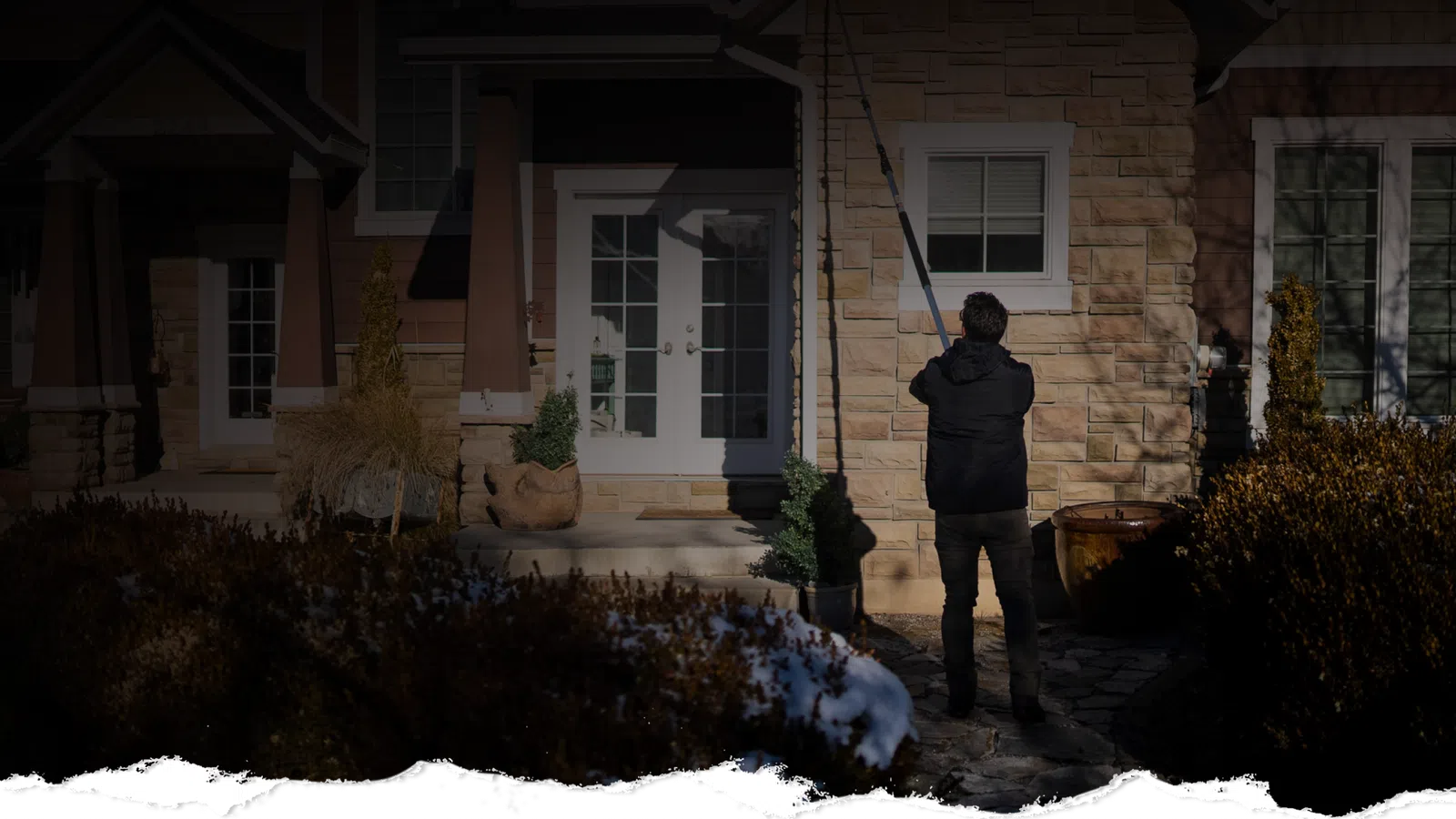 Person cleaning house exterior windows with a long pole washer on a sunny day.
