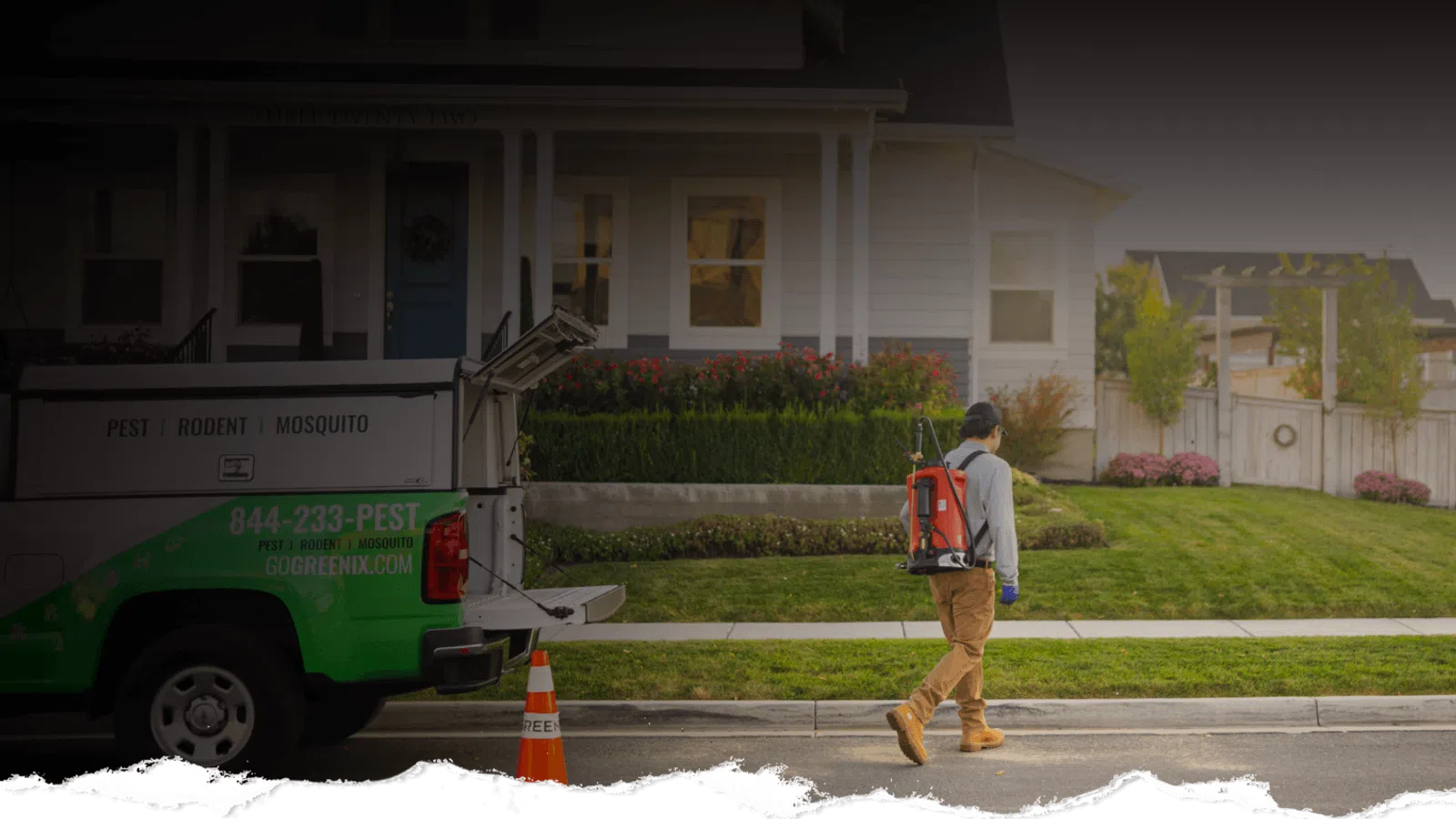 Pest control worker in protective gear walking near a green and white truck outside a suburban house.