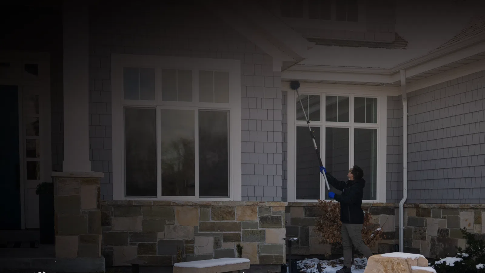 Person cleaning windows of a stone and shingles house during winter with snow on the ground