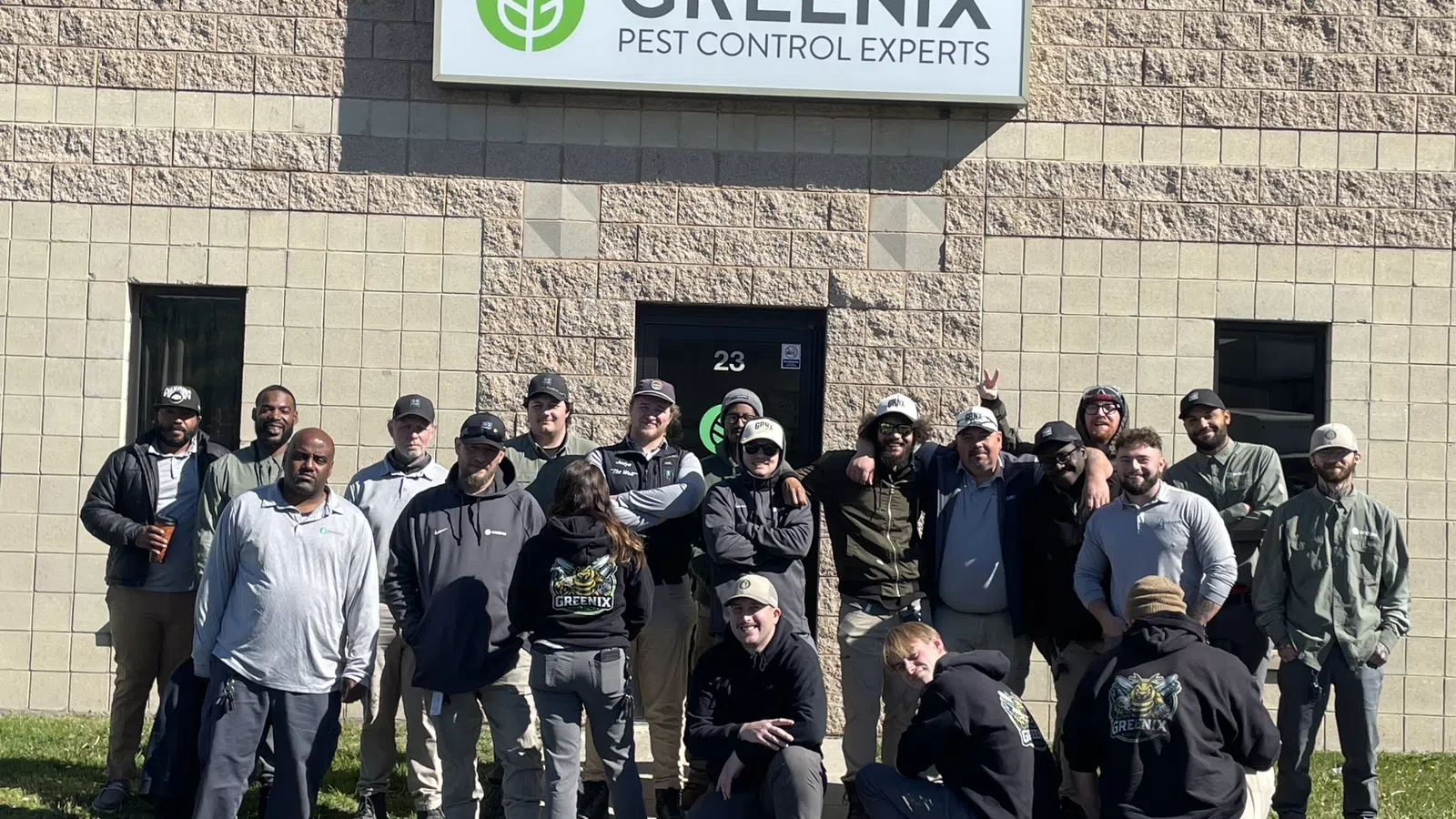 Group photo of Greenix Pest Control experts standing outside their office building under the company sign.