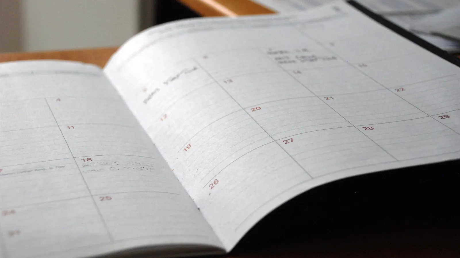 Close-up of an open monthly planner with dates and light handwritten notes on wooden desk