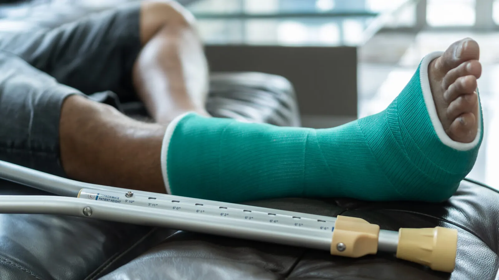 Person resting with a green leg cast and crutches on a leather couch after injury recovery.