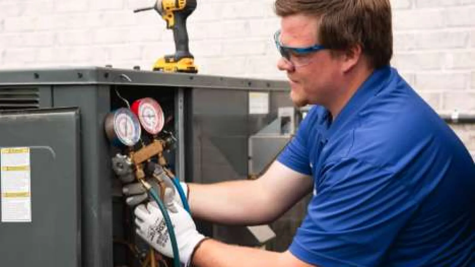Guardian Home Experts Technician in blue shirt and gloves servicing AC unit using pressure gauges and tools.