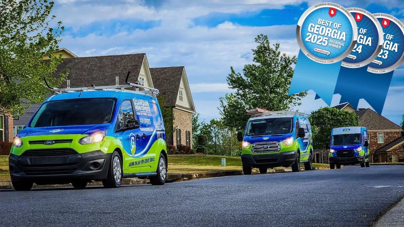 Three green and blue service vans parked on a suburban street with residential houses and Best of Georgia award ribbons.