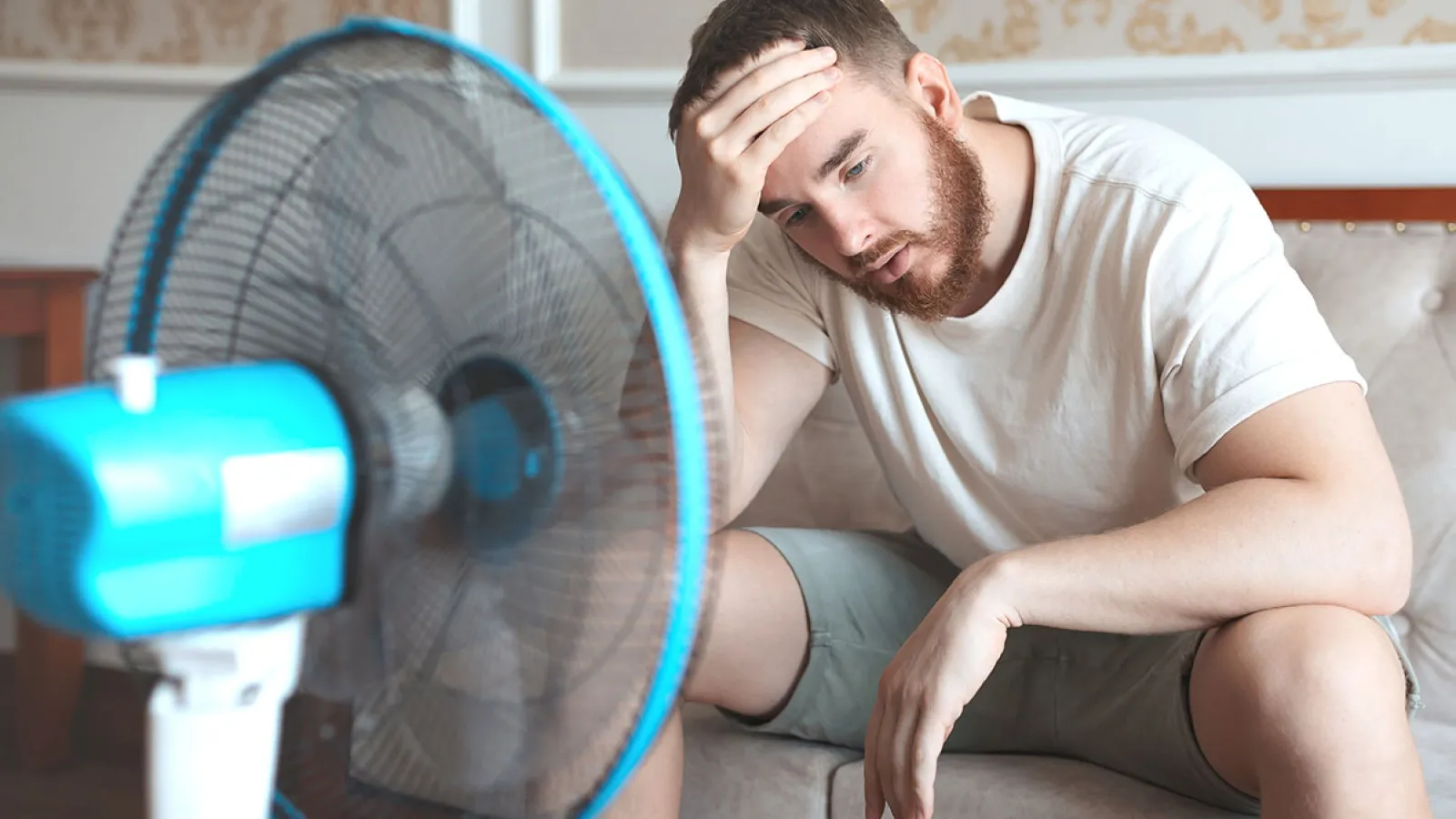 A man looking frustrated sitting near a fan in a warm room