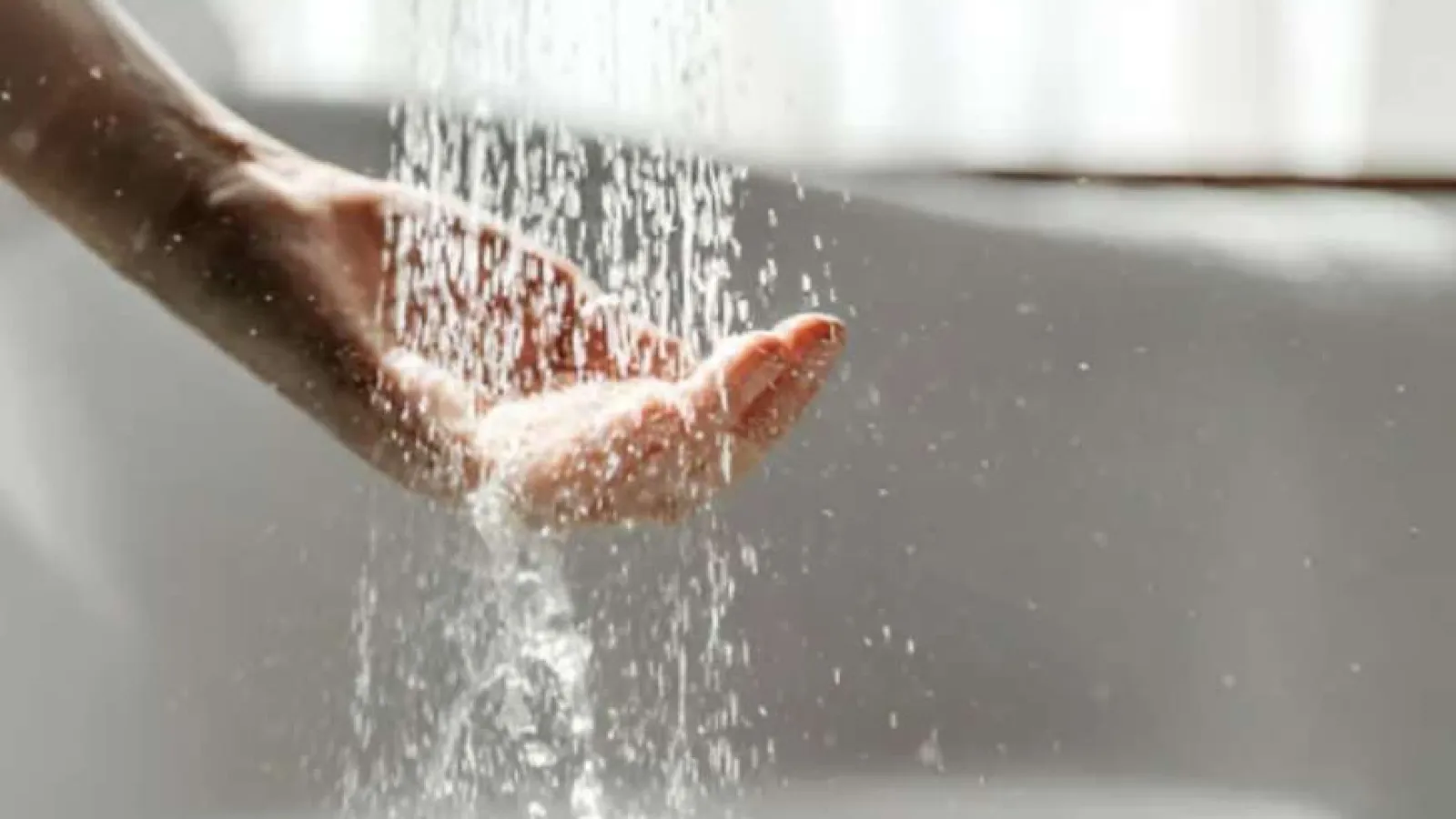 Close-up of a hand catching water droplets flowing from above against a blurred background.
