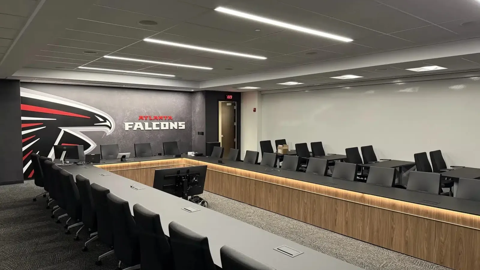 Modern conference room with Atlanta Falcons logo on wall, sleek black chairs, wood paneling, and U-shaped tables.