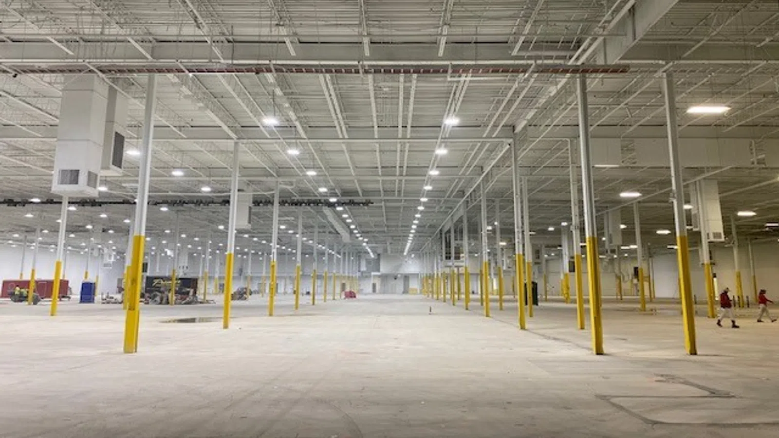 Spacious empty warehouse interior with high ceiling, yellow safety poles, and bright overhead lighting