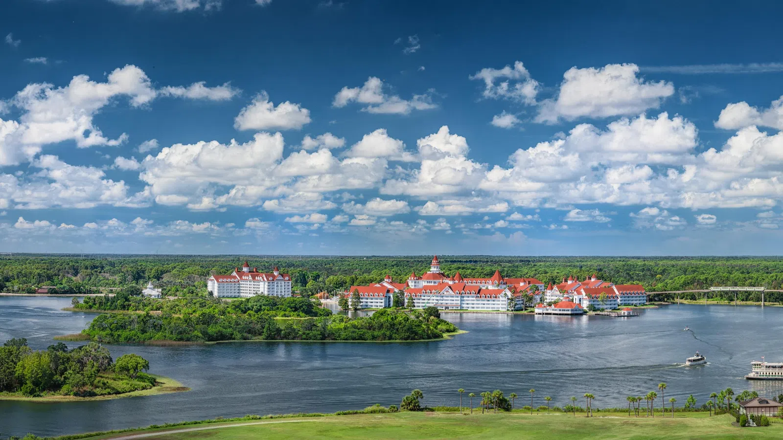 Panoramic view of a resort with red roofs surrounded by water, islands, and lush greenery under a blue sky with clouds