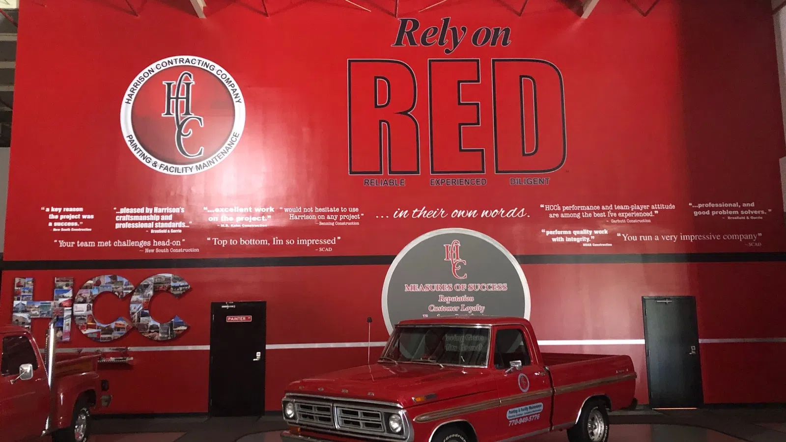 Vintage red pickup truck inside a red wall with Harrison Contracting Company branding and slogans.