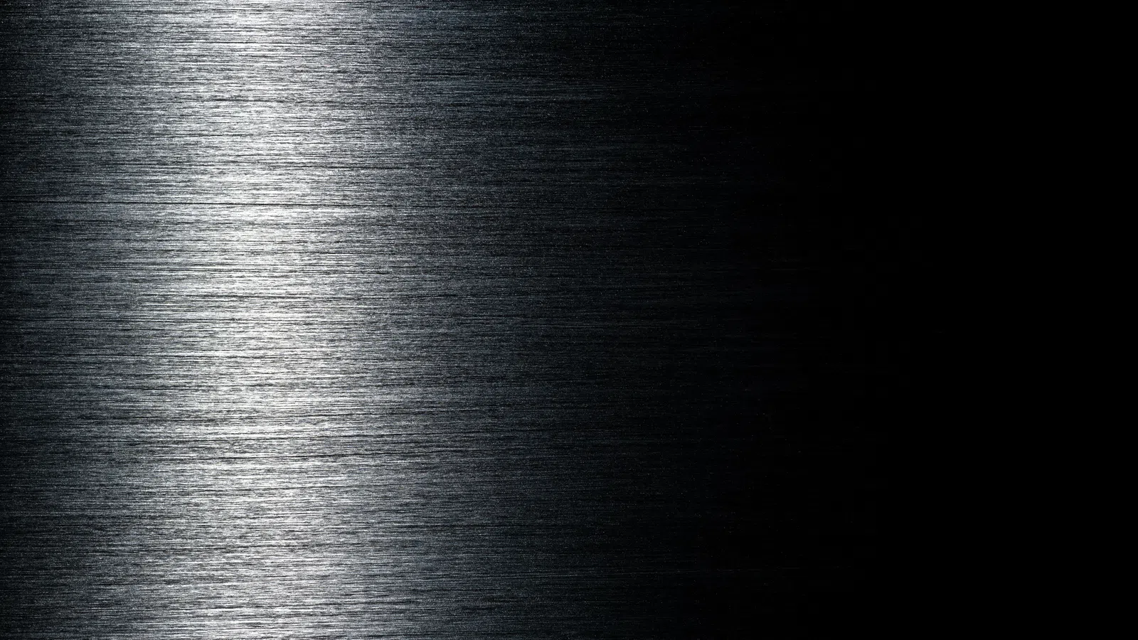Close-up of brushed metal surface with gradient lighting from bright silver to deep black shadow.