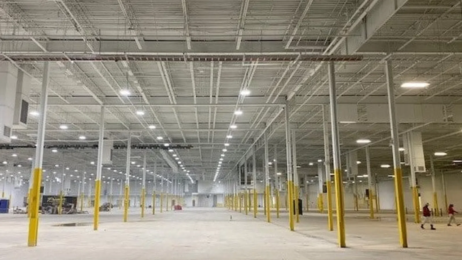 Wide interior of an empty warehouse with yellow support columns and bright overhead lighting