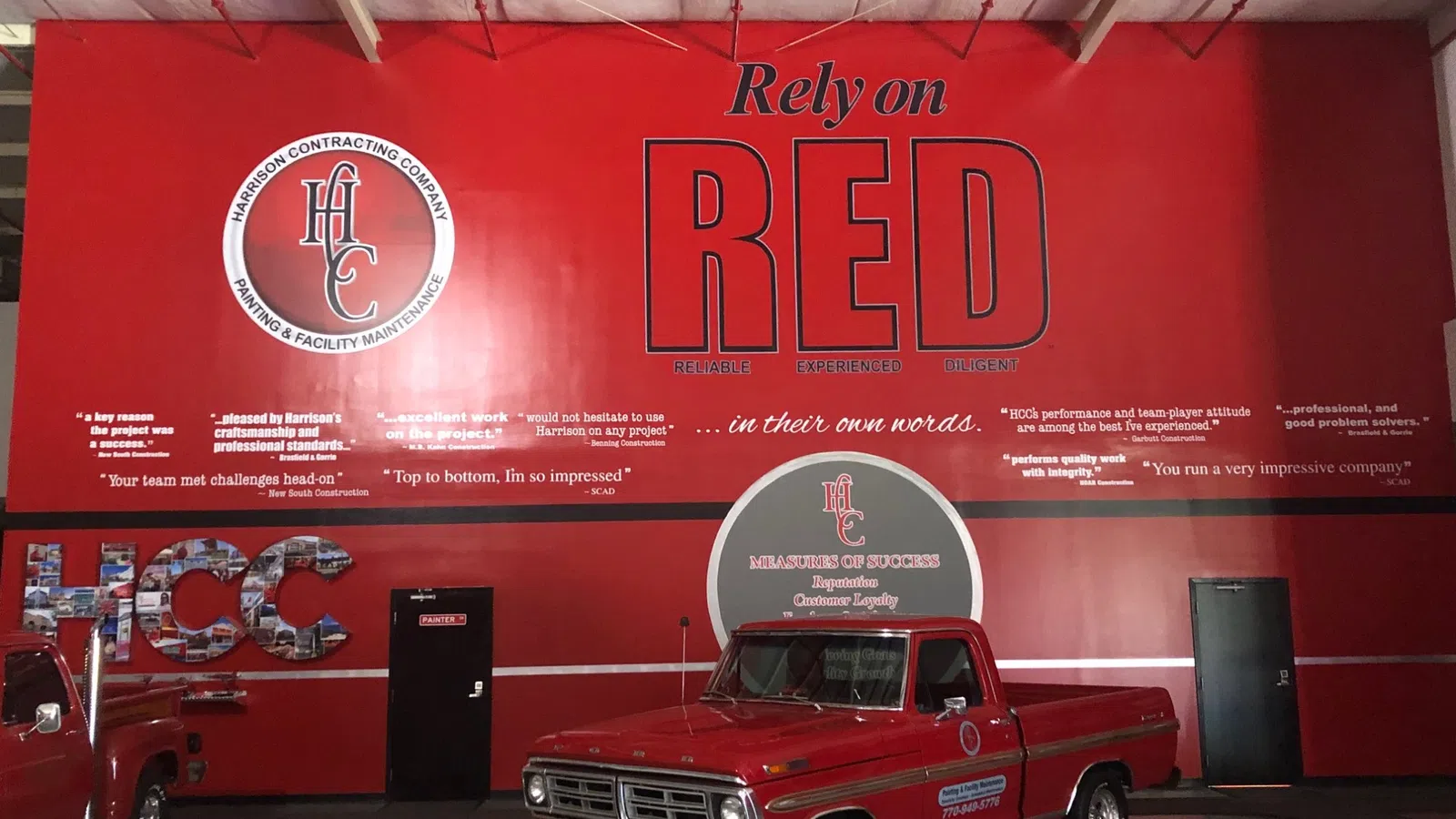 Vintage red pickup truck inside a red wall with Harrison Contracting Company branding and slogans.