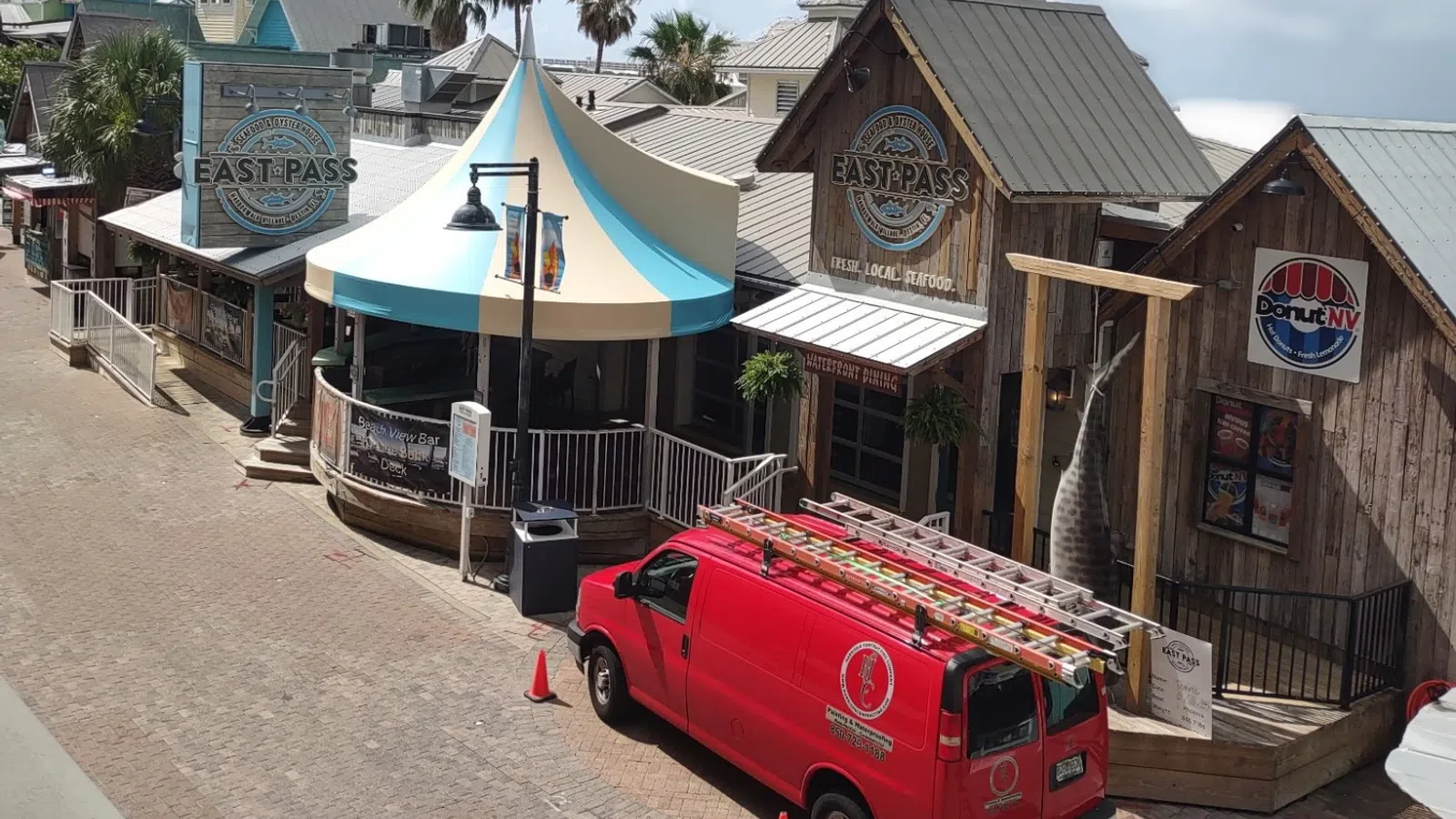 Street view of rustic shops including East Pass Seafood and a red service van parked outside on a sunny day.