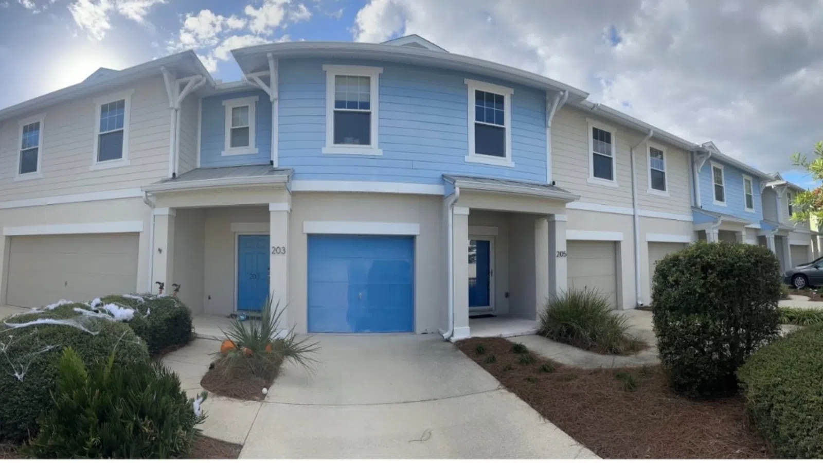 Row of modern two-story townhouses with blue and beige siding and attached garages under a cloudy sky.