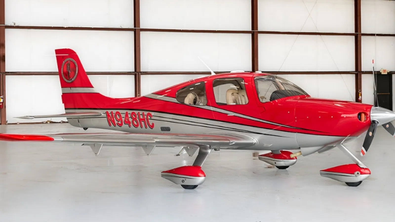 Red and silver single-engine private airplane in a spacious hangar with registration N948HC visible.