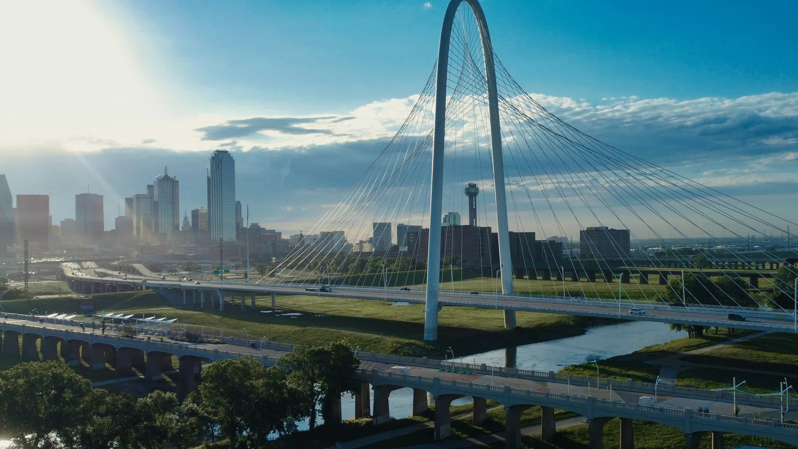 Dallas city skyline with Margaret Hunt Hill Bridge over the Trinity River at sunrise with scattered clouds and blue sky.