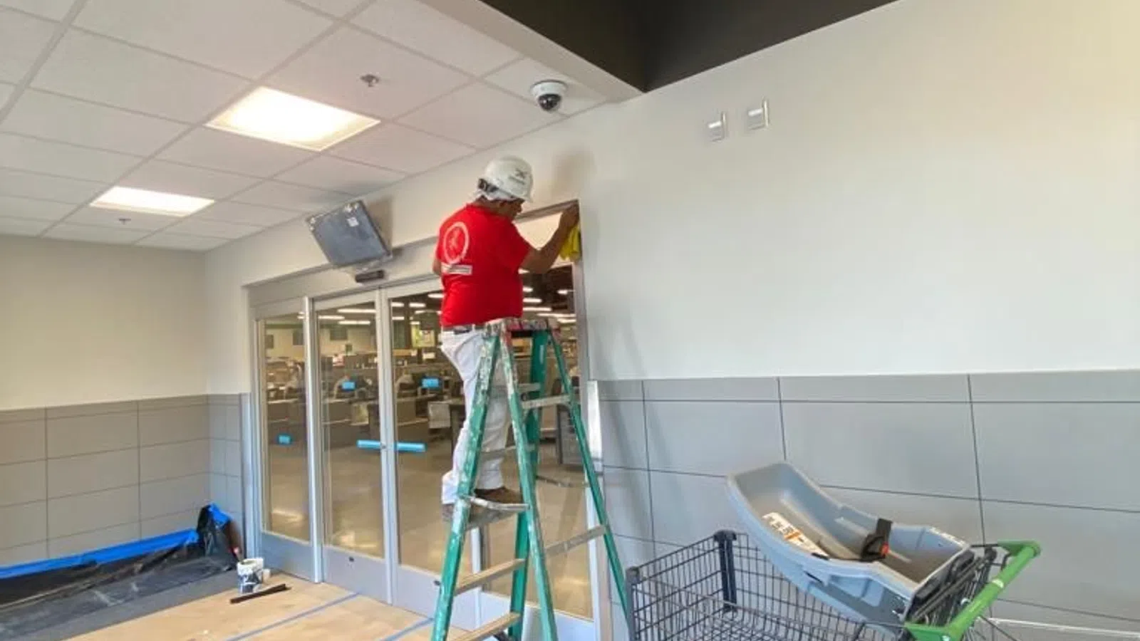 Worker in red shirt on ladder installing or cleaning near entrance doors of a commercial building under construction.