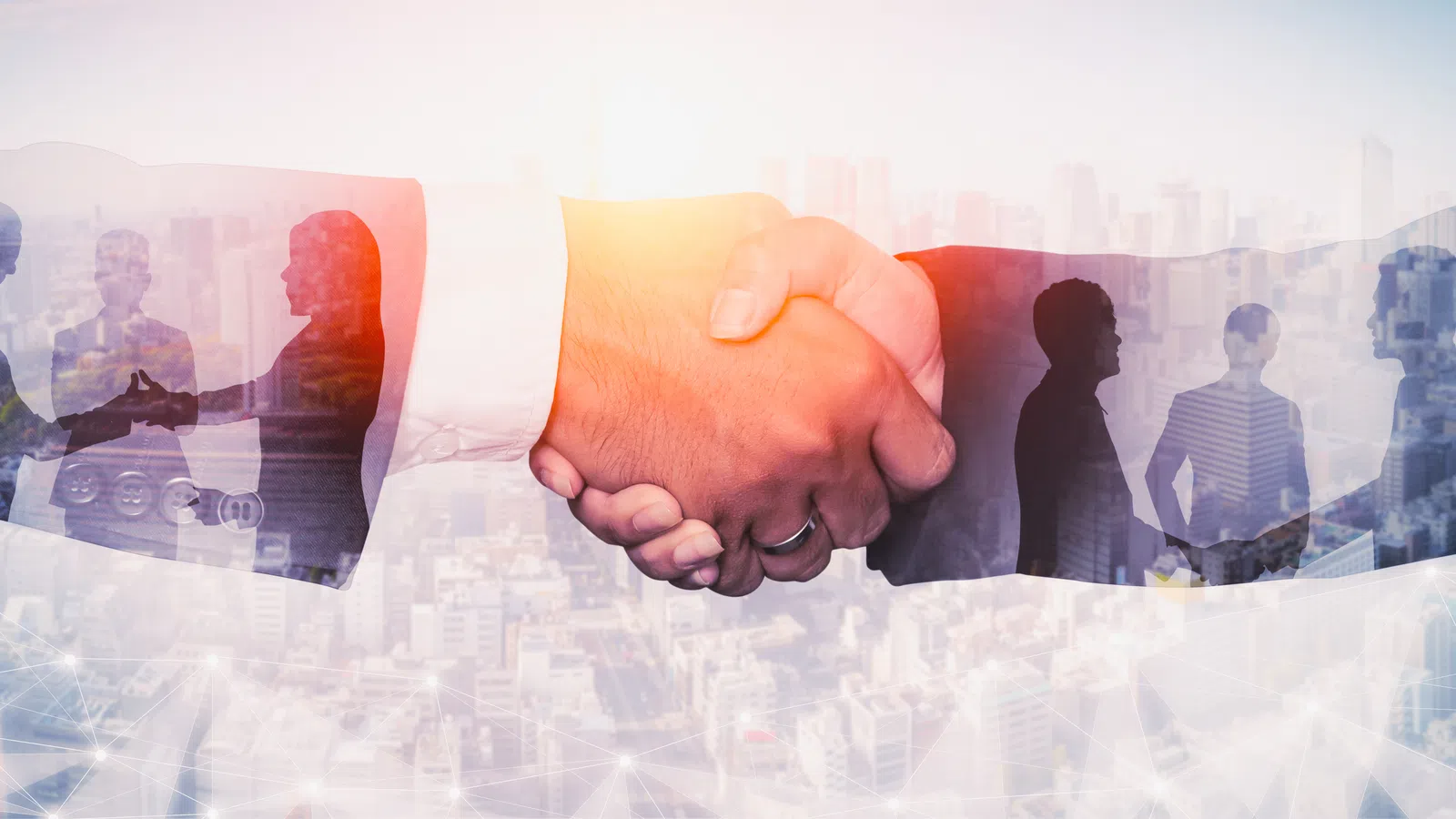 Close-up of business handshake with cityscape and silhouettes of people collaborating in background.