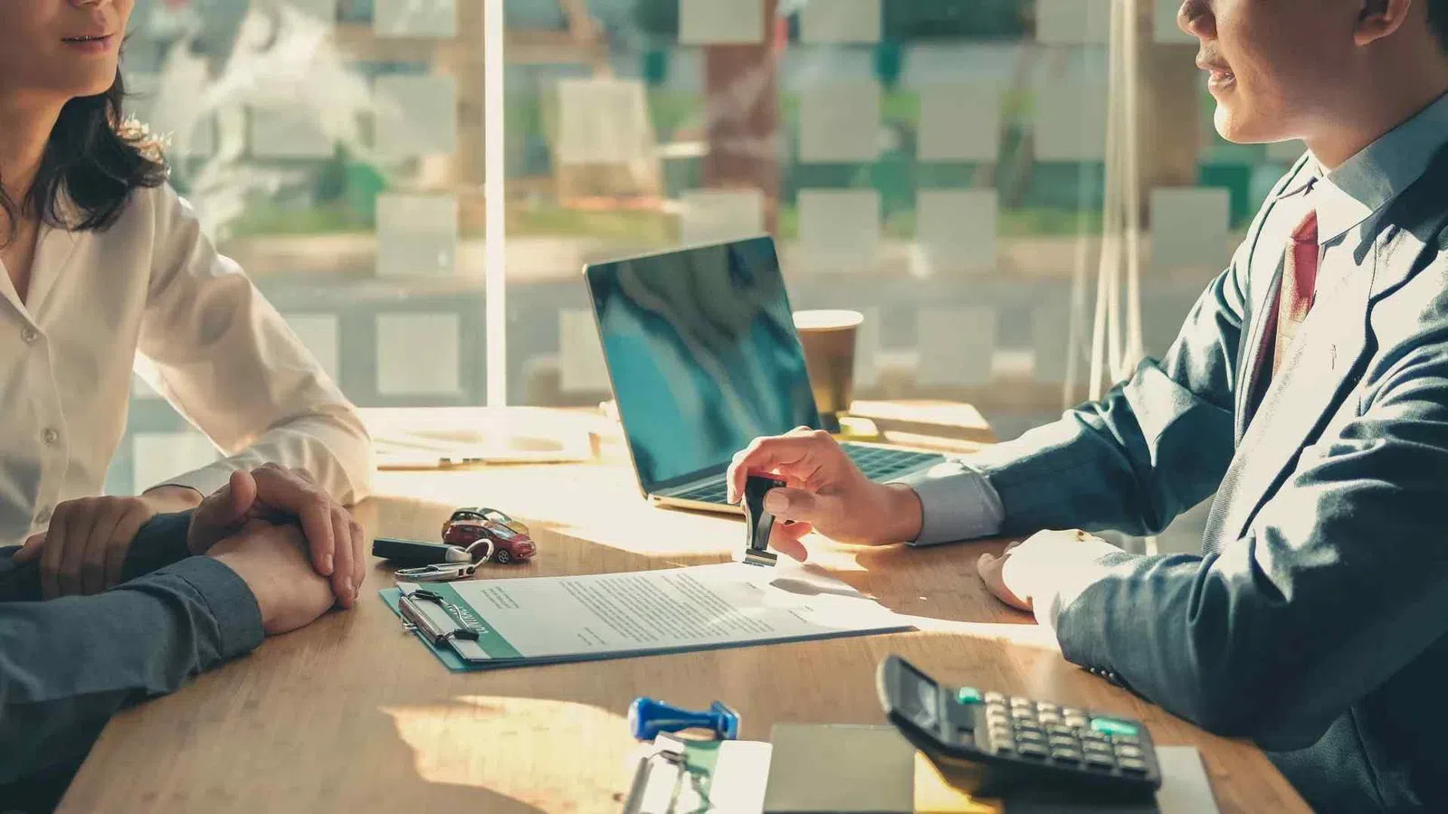 Business professional stamping a contract document at a meeting with two clients in a sunlit office.