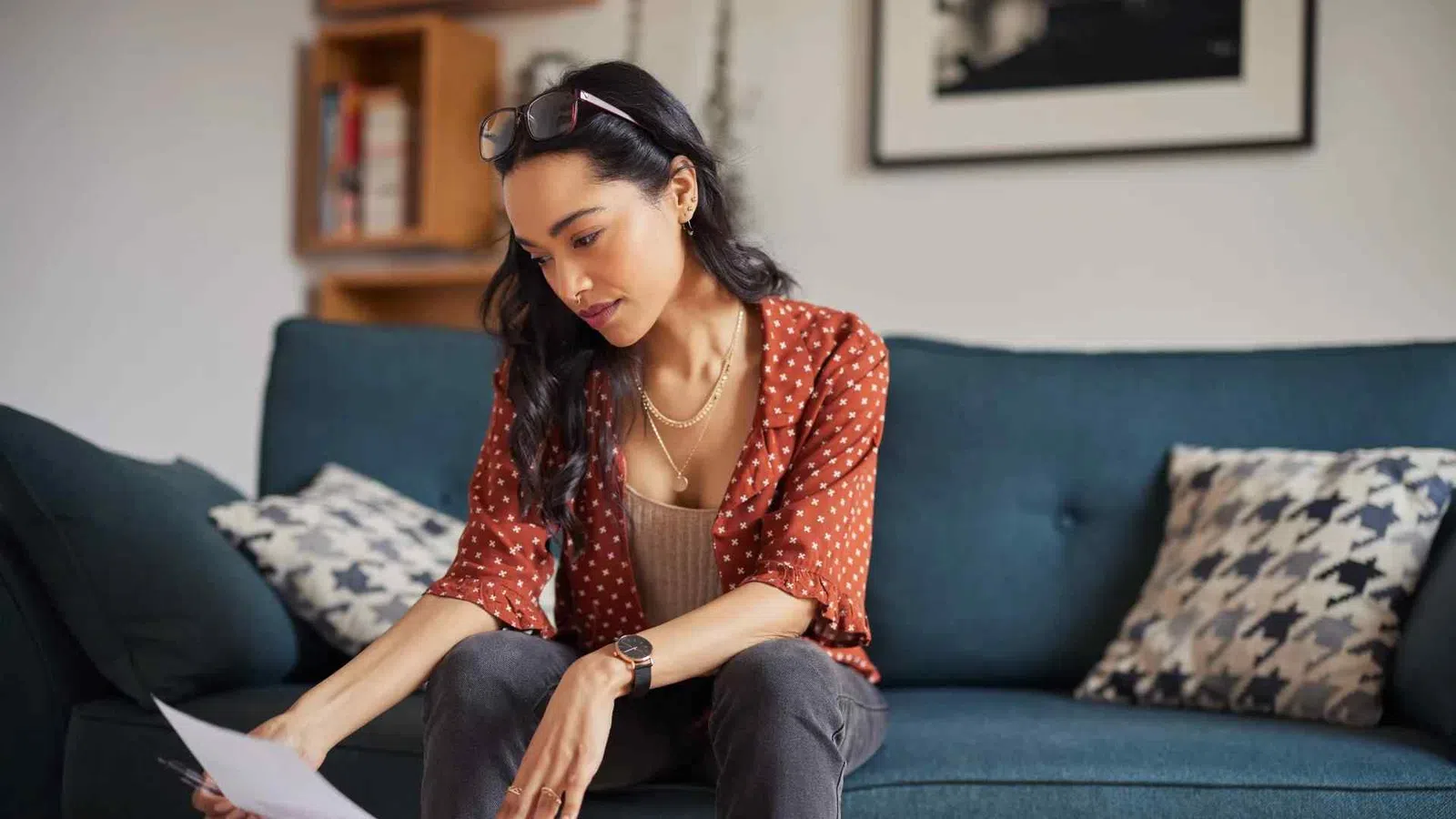 Young woman in casual outfit sitting on blue couch reading documents attentively in cozy living room.