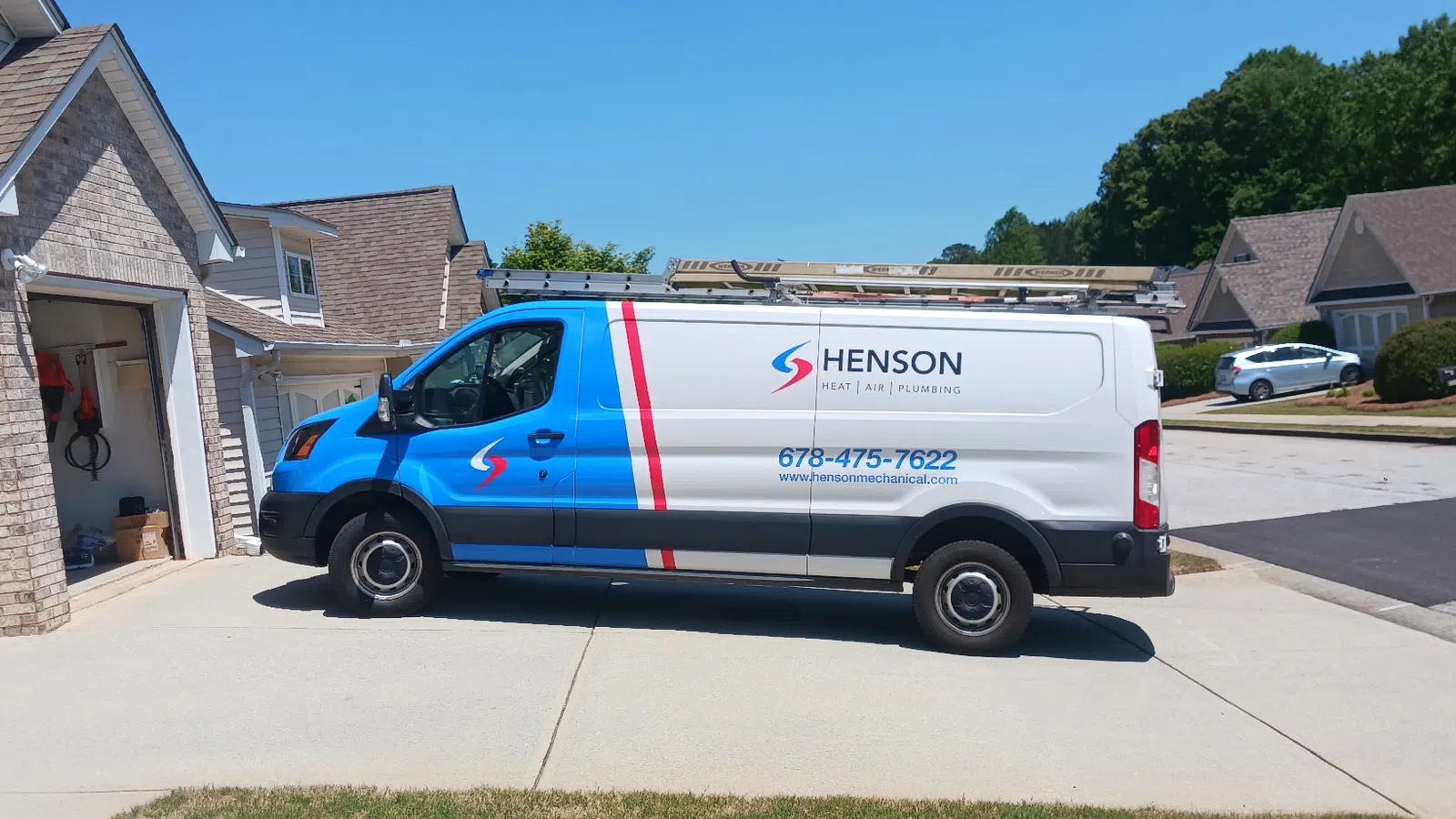 Henson Mechanical Heating Air and Plumbing service van parked in a suburban driveway on a sunny day with houses and trees in the background
