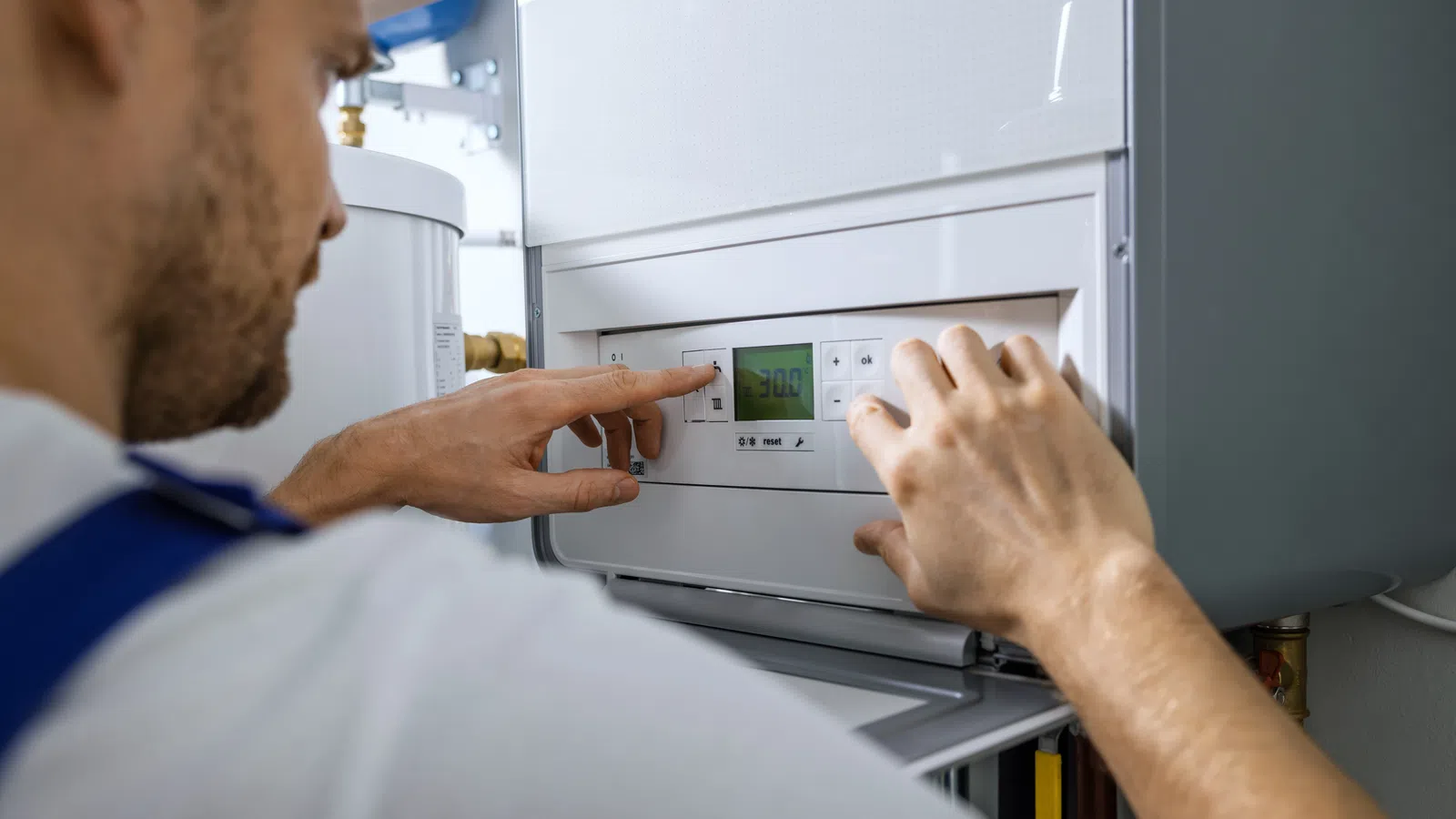 Technician adjusting settings on a modern wall-mounted boiler with digital display showing 30.0 degrees.