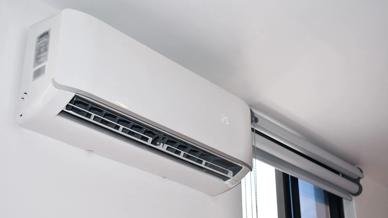 Modern white wall-mounted air conditioner unit displaying temperature 25 installed near window.