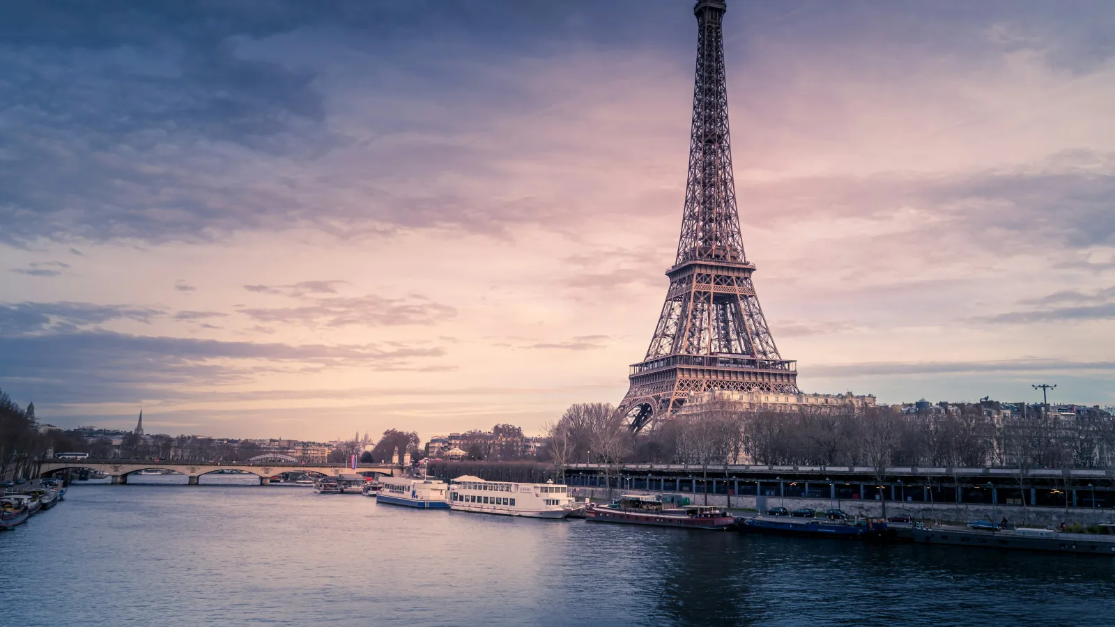 Eiffel Tower overlooking the Seine River with boats and a sunset sky in Paris, France.