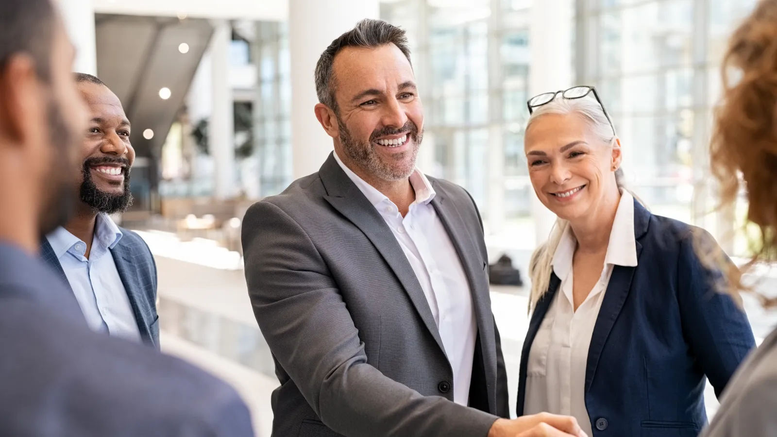 Business professionals smiling and shaking hands in a modern office setting during a meeting.