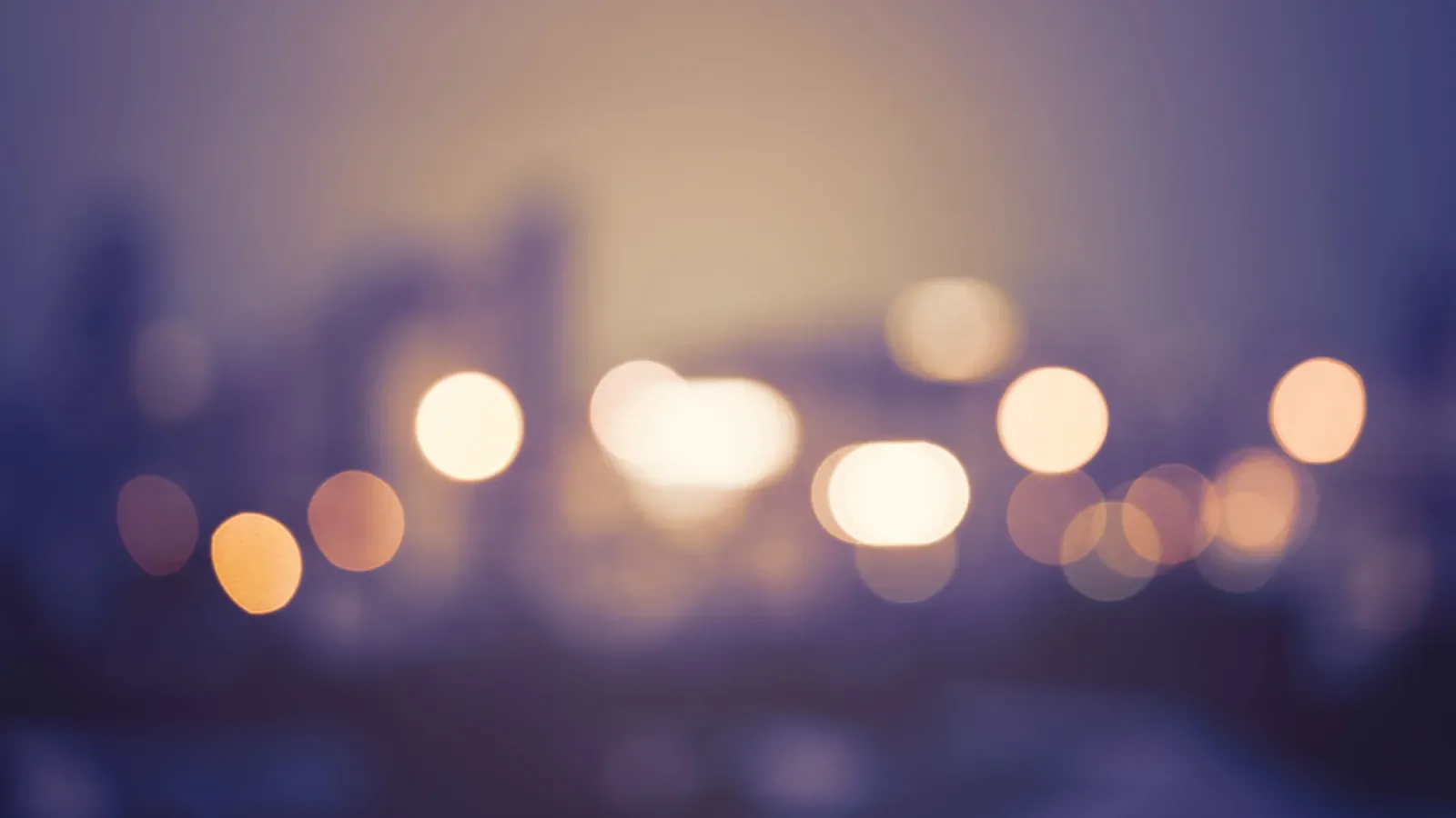 Blurred cityscape with glowing bokeh lights against a dusky sky in soft purple and orange tones