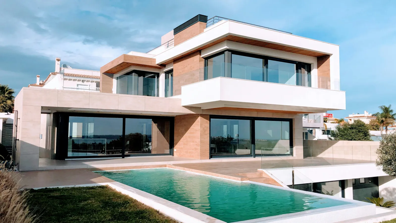 Modern two-story house with large glass windows and a rectangular swimming pool on a bright day.