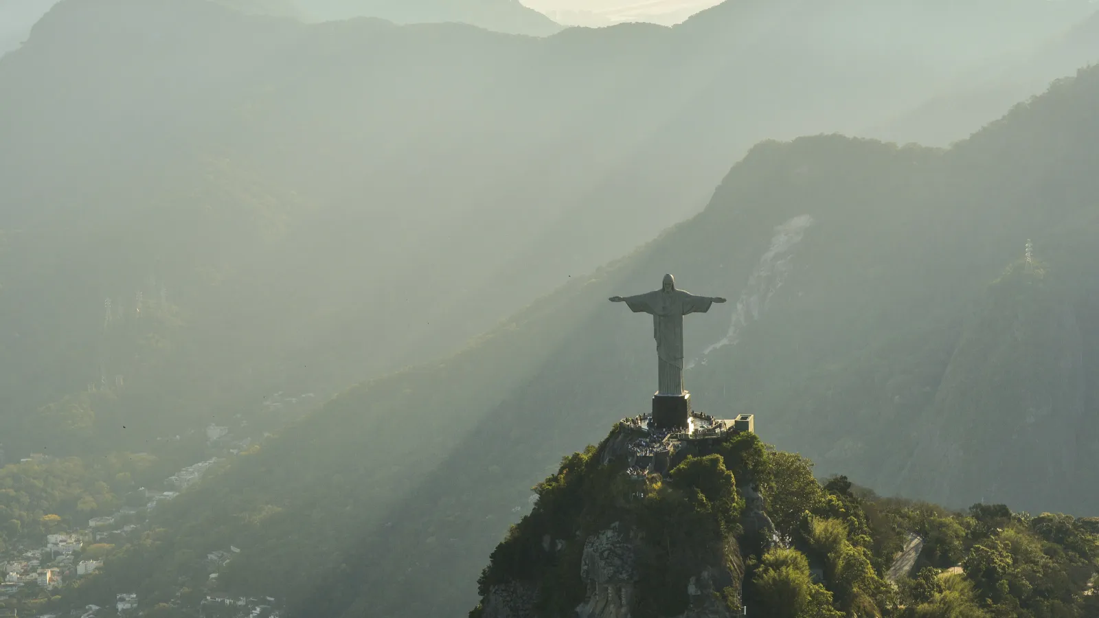 Christ the Redeemer statue atop Corcovado Mountain with sun rays and misty mountains in Rio de Janeiro.